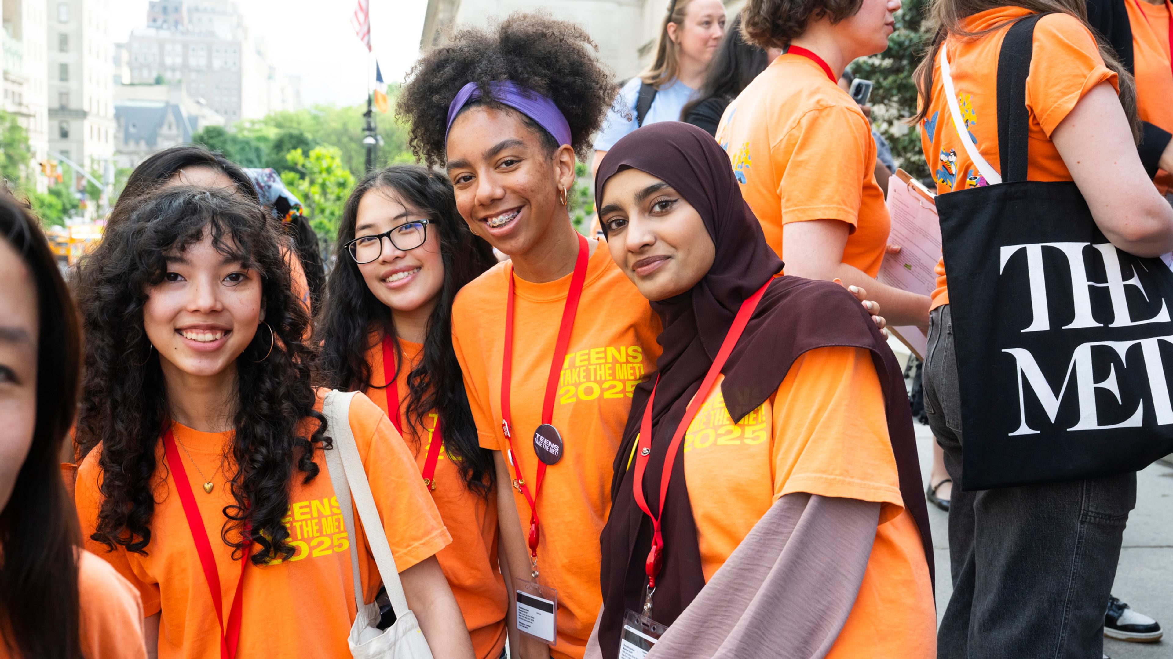 Group of teens in bright orange shirts posing for a photo on the steps of The Met