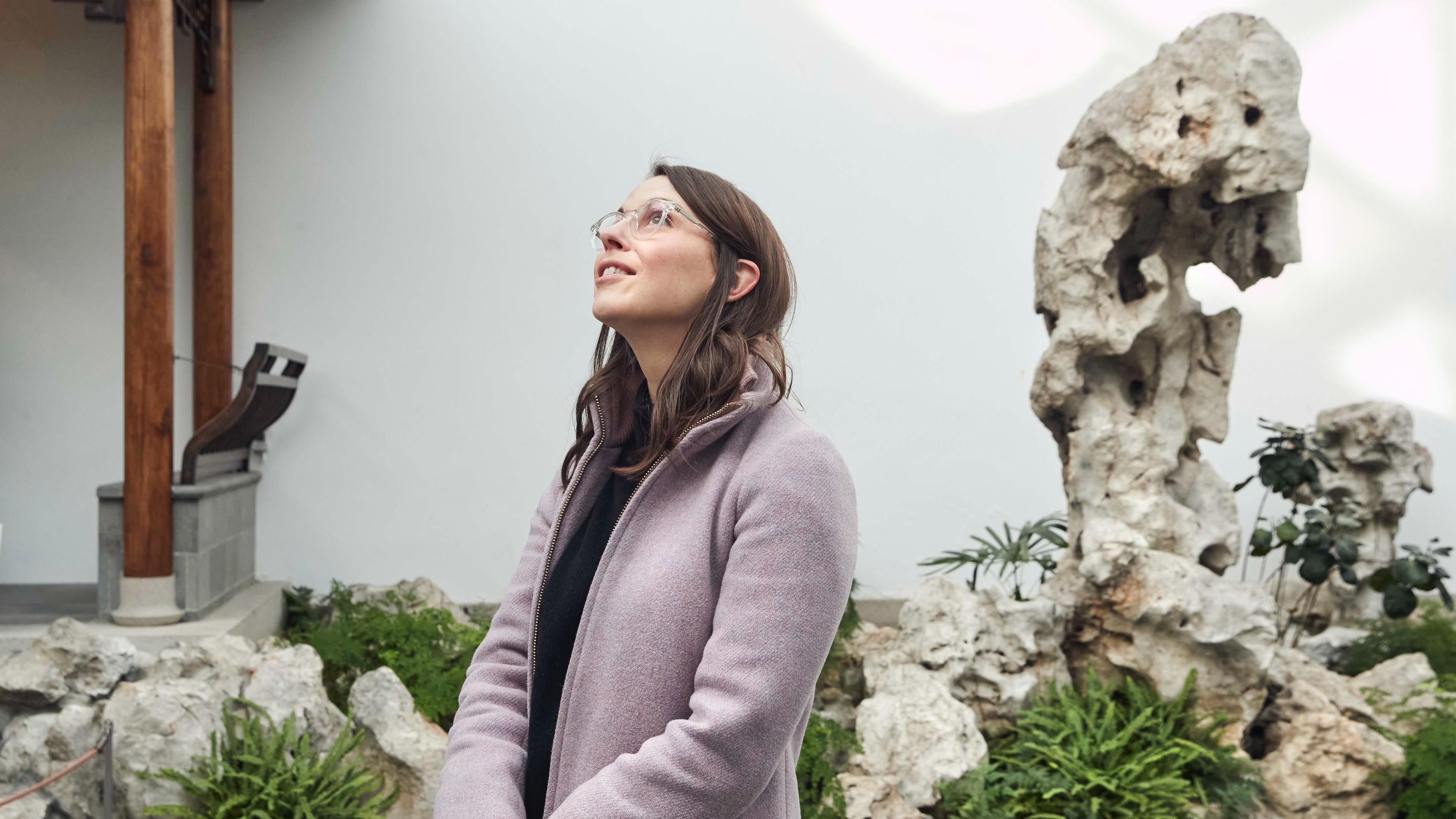 Image of woman in a grey jacket standing in The Met's Astor Court.