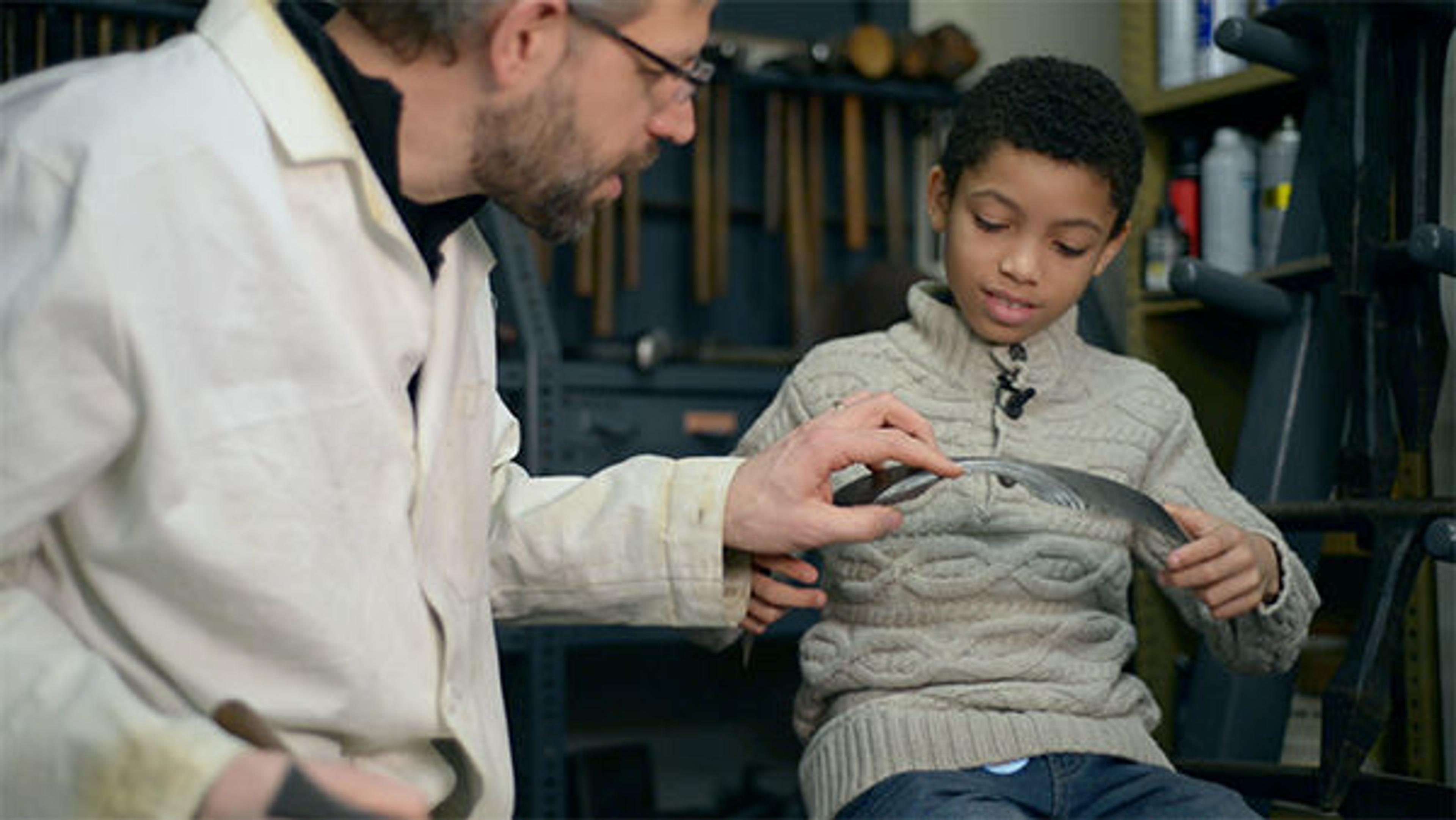 A boy looks at a piece of armor with a conservator