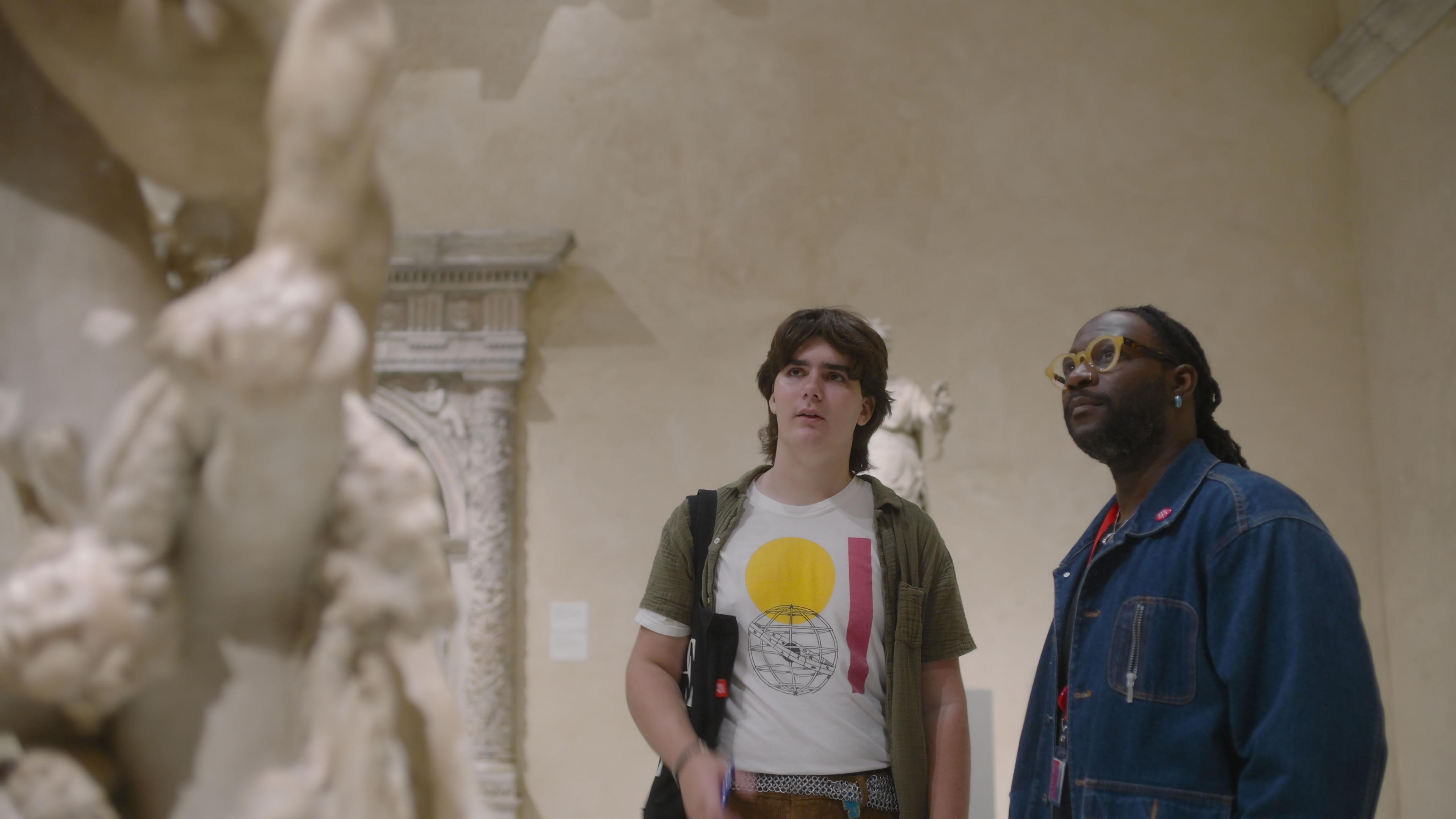 A teenage Met Intern wearing a white t-shirt with a yellow circle and red line stands next to his mentor, Jeary Payne.