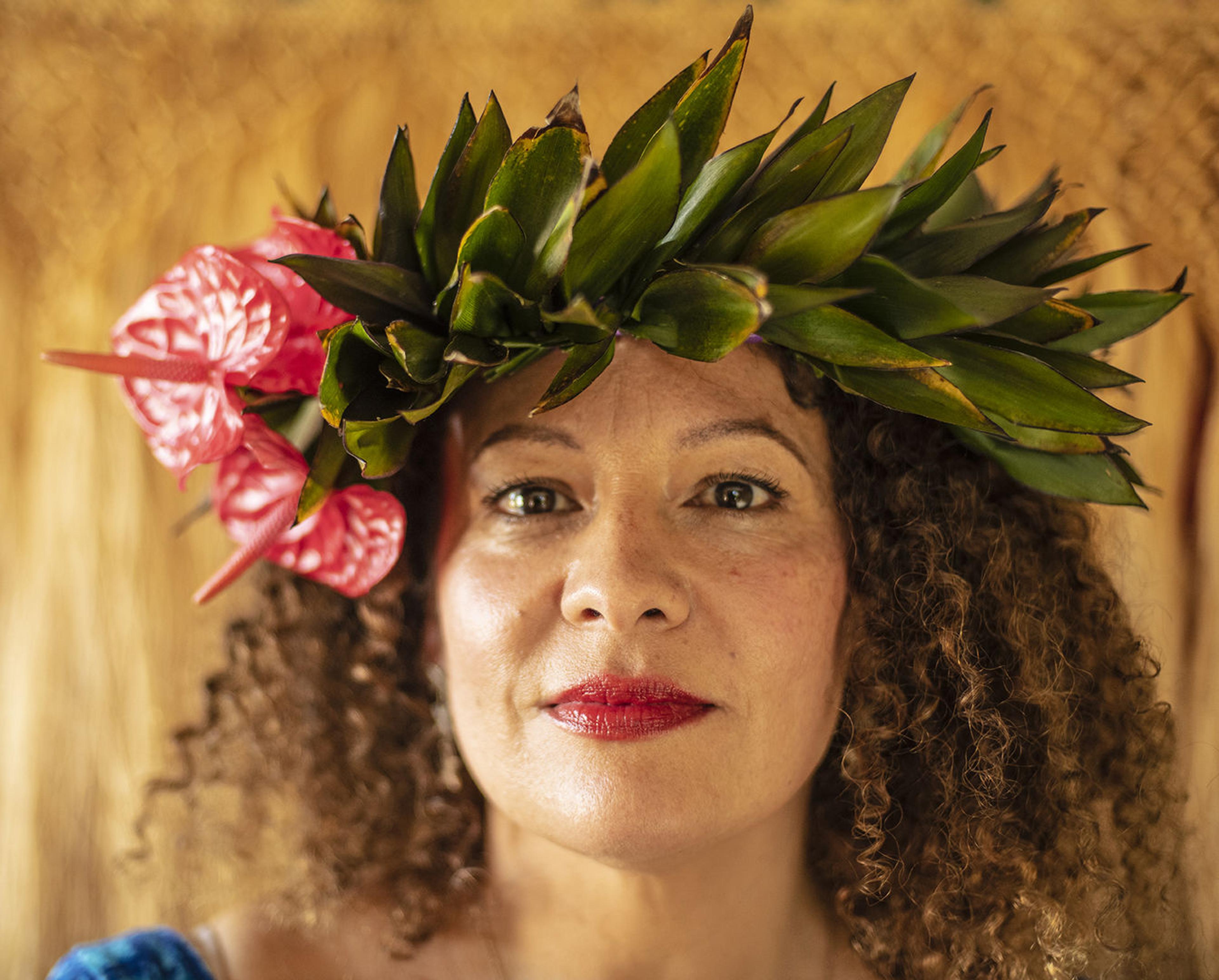 Portrait of a woman with shoulder length curly hair, red lipstick, and a headdress of plants and flowers