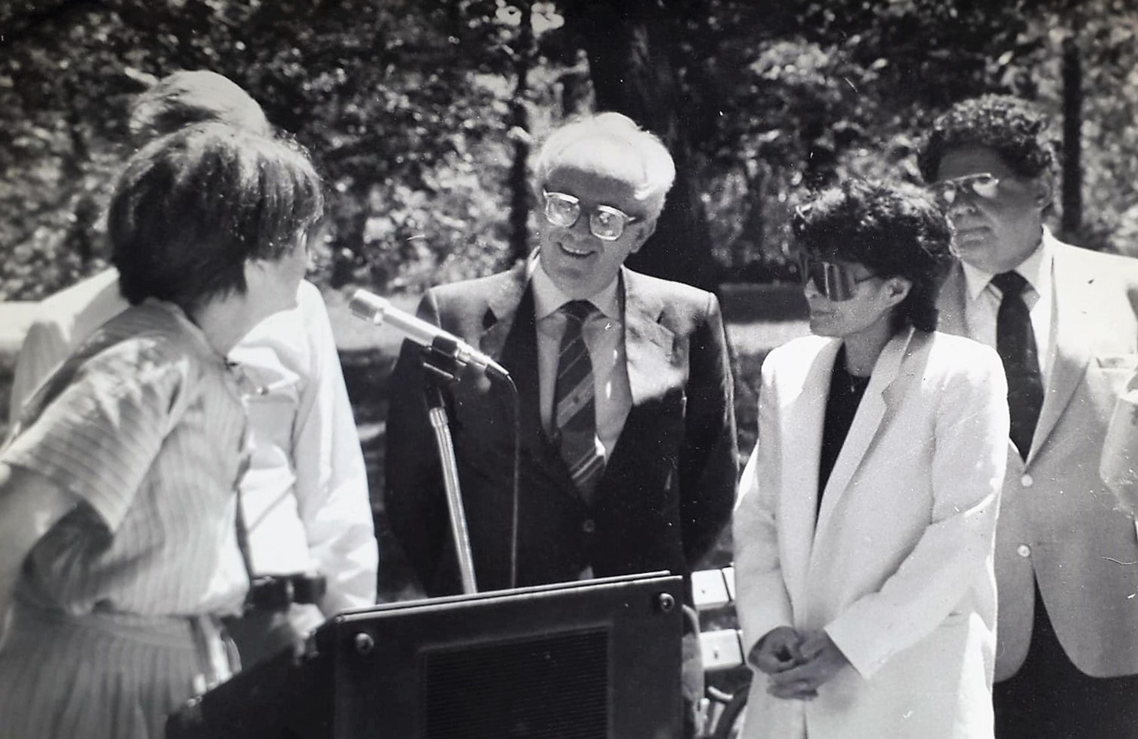 Black and white photo of 3 men and two women standing beside a podium