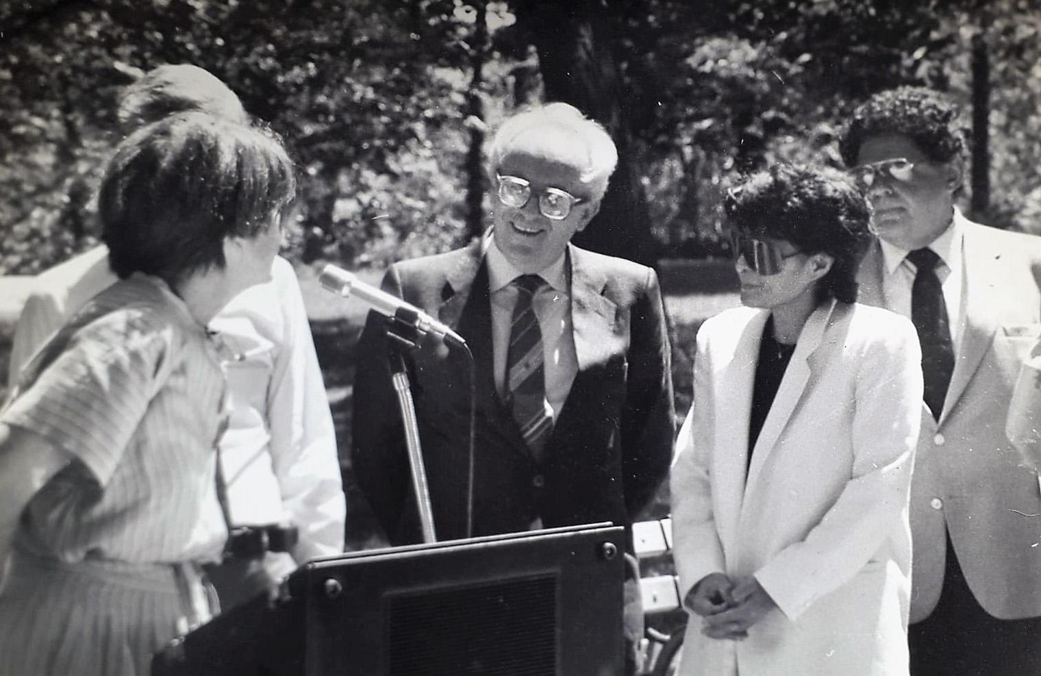 Black and white photo of 3 men and two women standing beside a podium