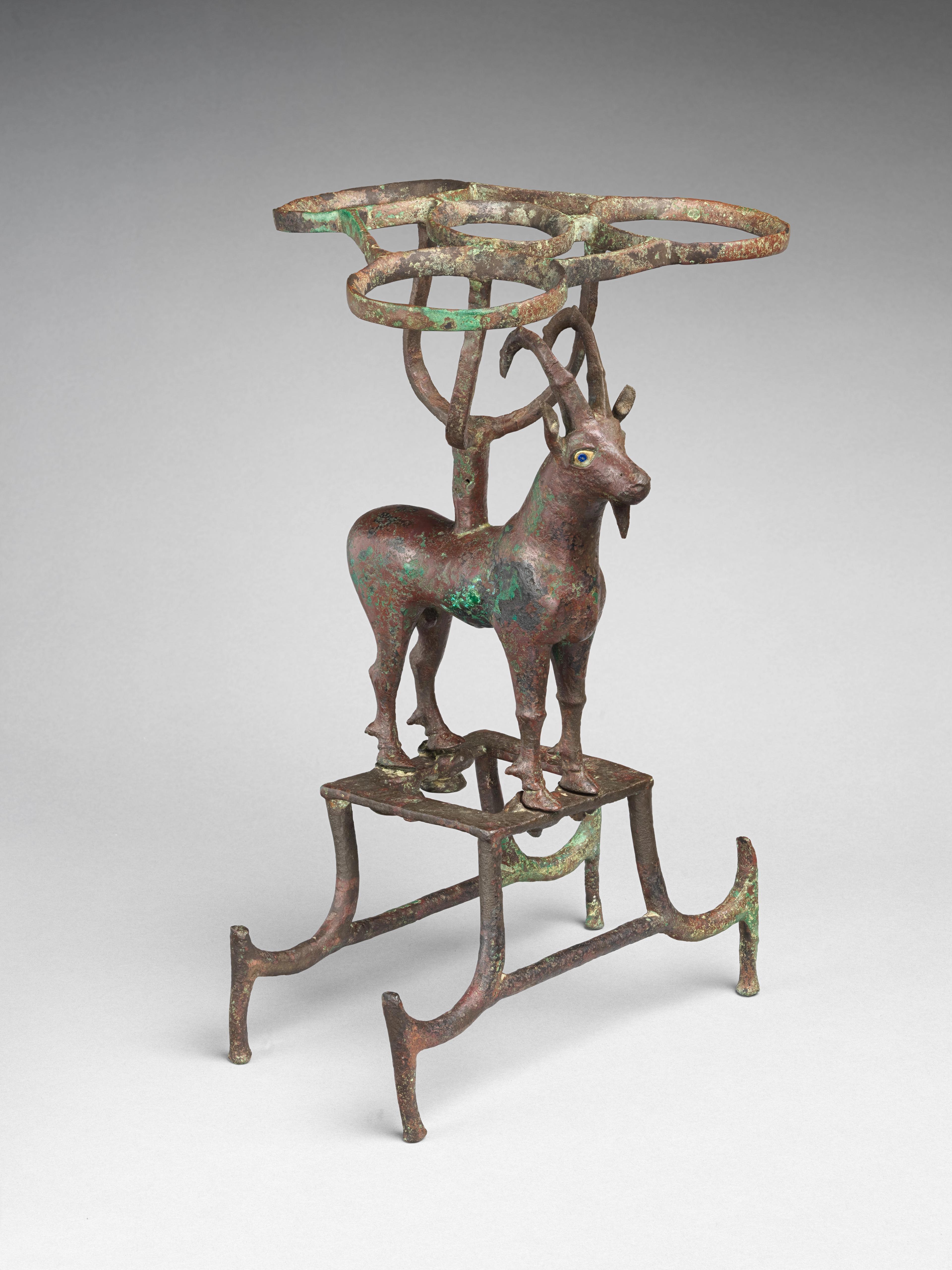 Copper stand comprised of an ibex with supports for vessels on its back and below its feet. The sculpture shows some green oxidation.