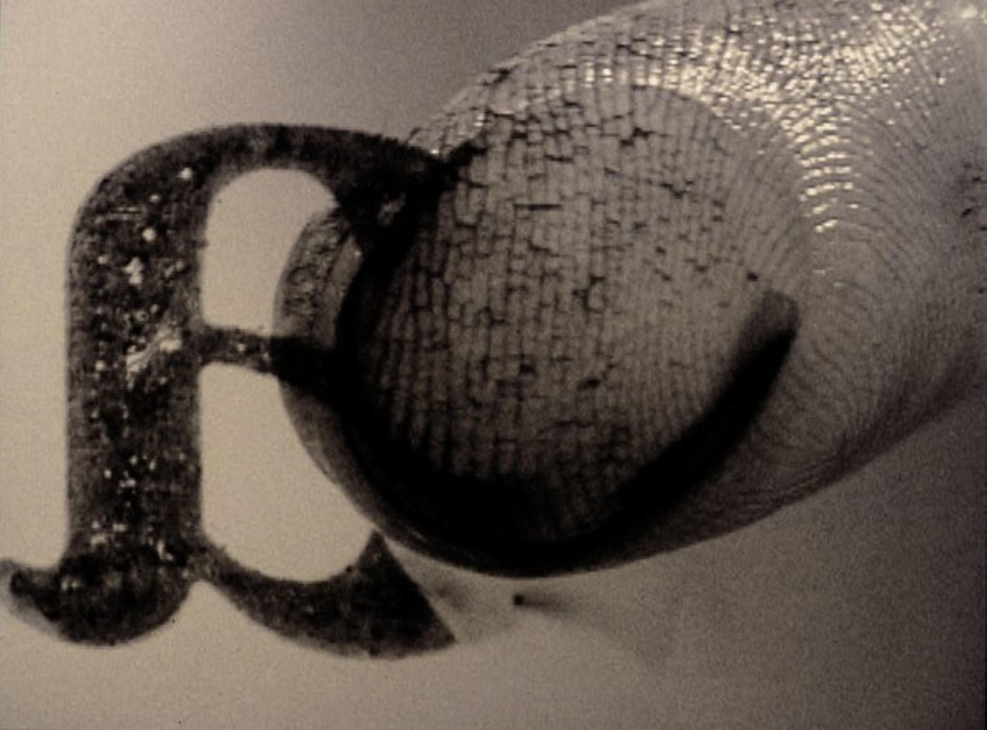 Video still of a close-up of a finger with black ink on it and a backwards letter
