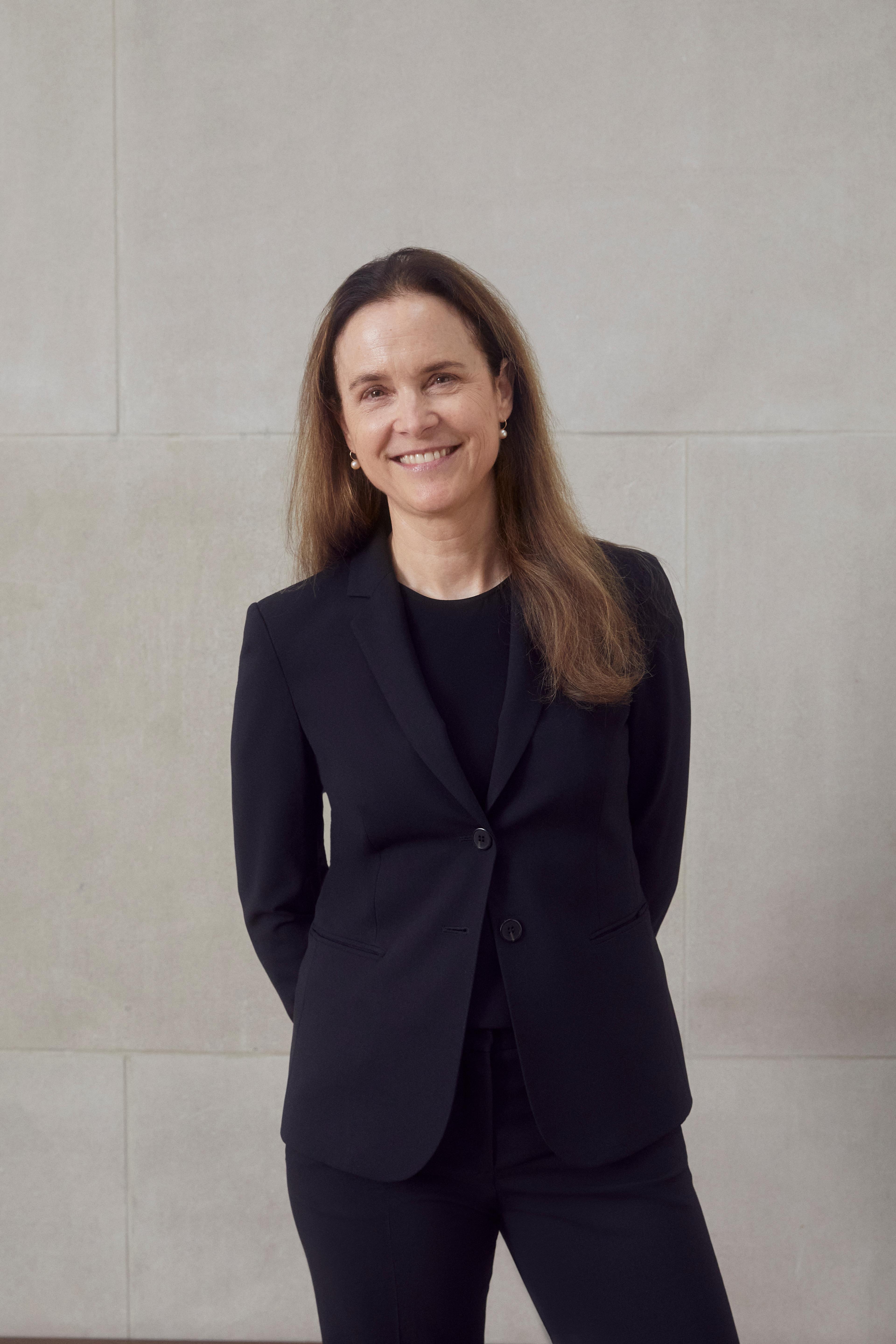 A color photograph of Quincy Houghton standing in front of a stone wall in a black suit.