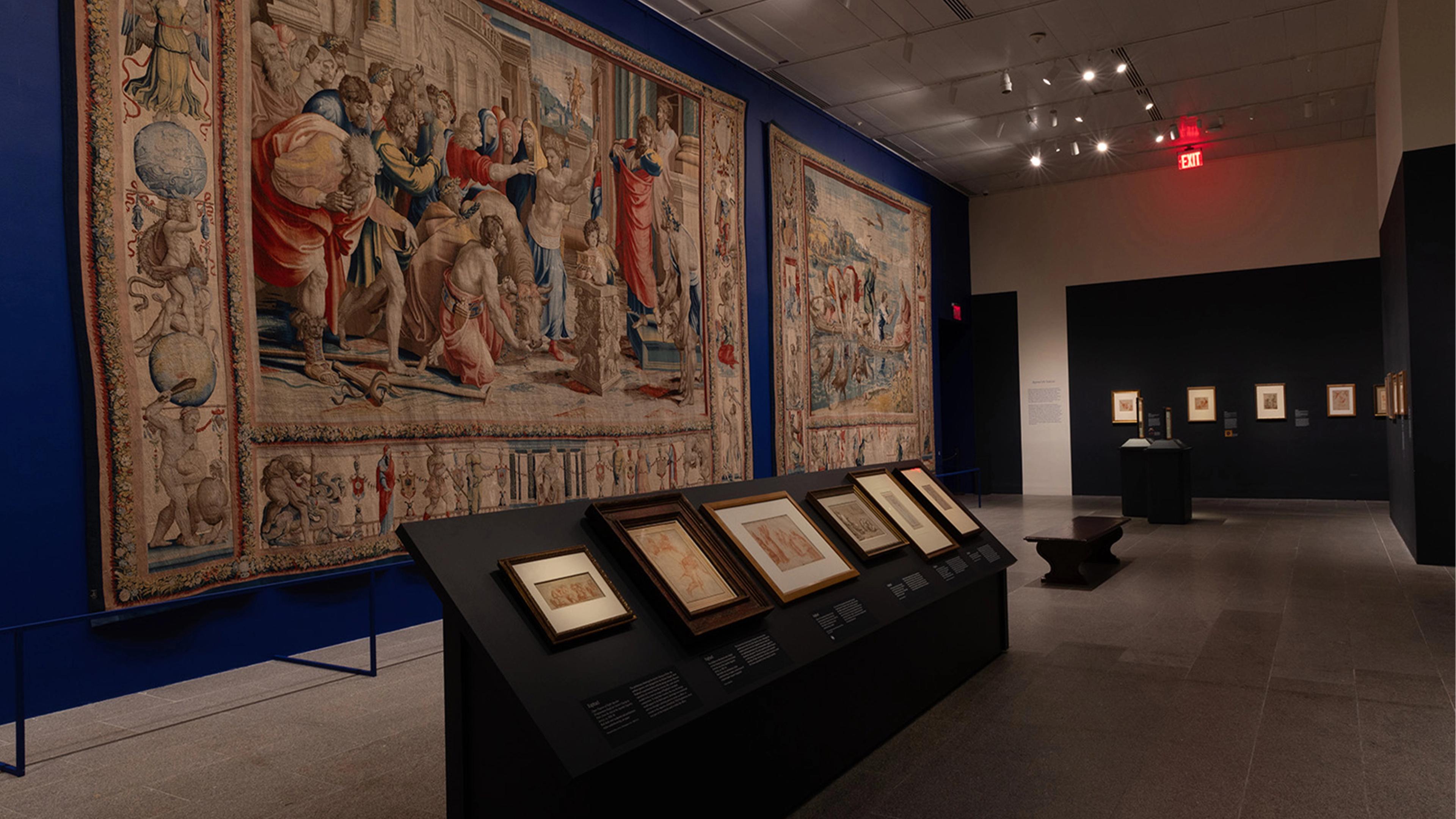 Museum gallery with large, intricate tapestries featuring historical scenes on the walls.