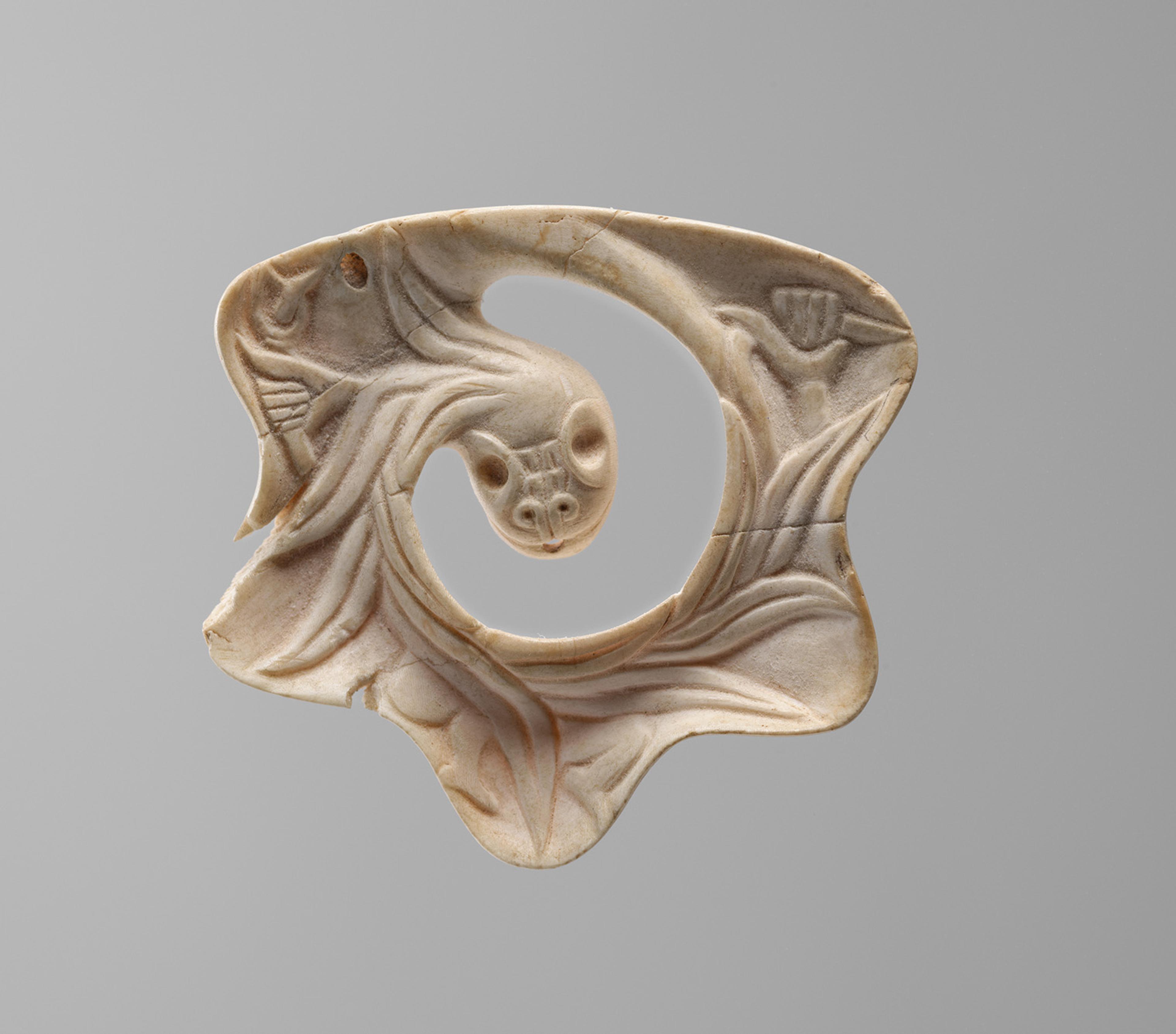 ntricately carved jade ornament with swirling patterns, featuring a central animal head with large eyes, set on a neutral gray background.