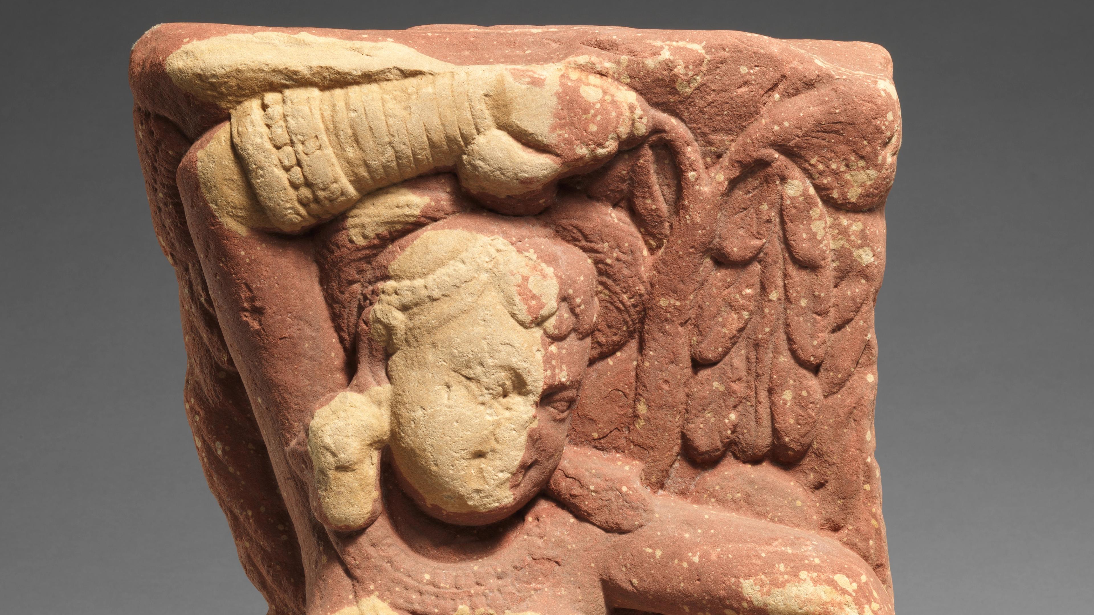 A sandstone figure with detailed garments and carved wings