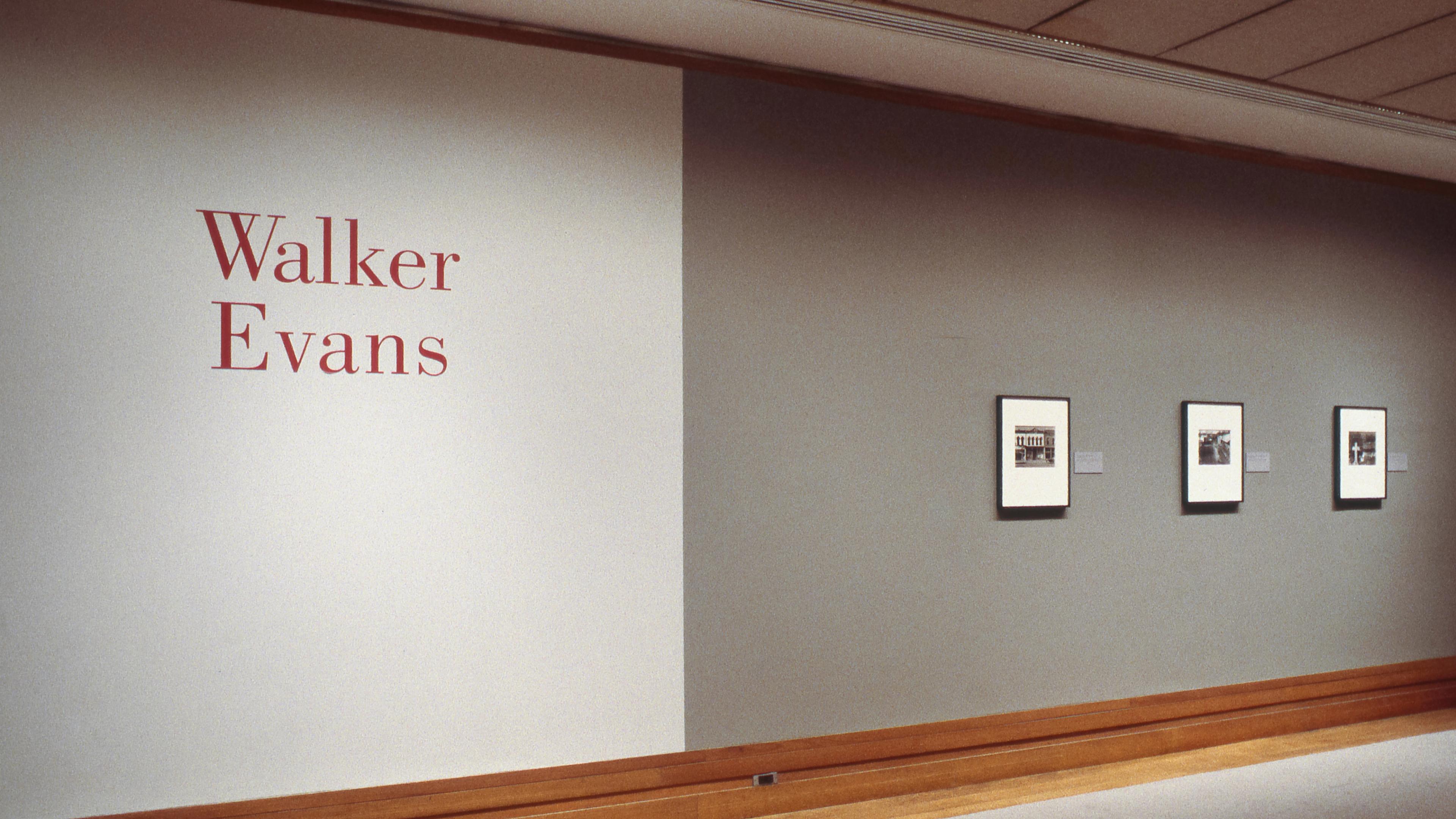 Red wall text reading "Walker Evans" against a white background, next to a gray wall panel with three frame photos.