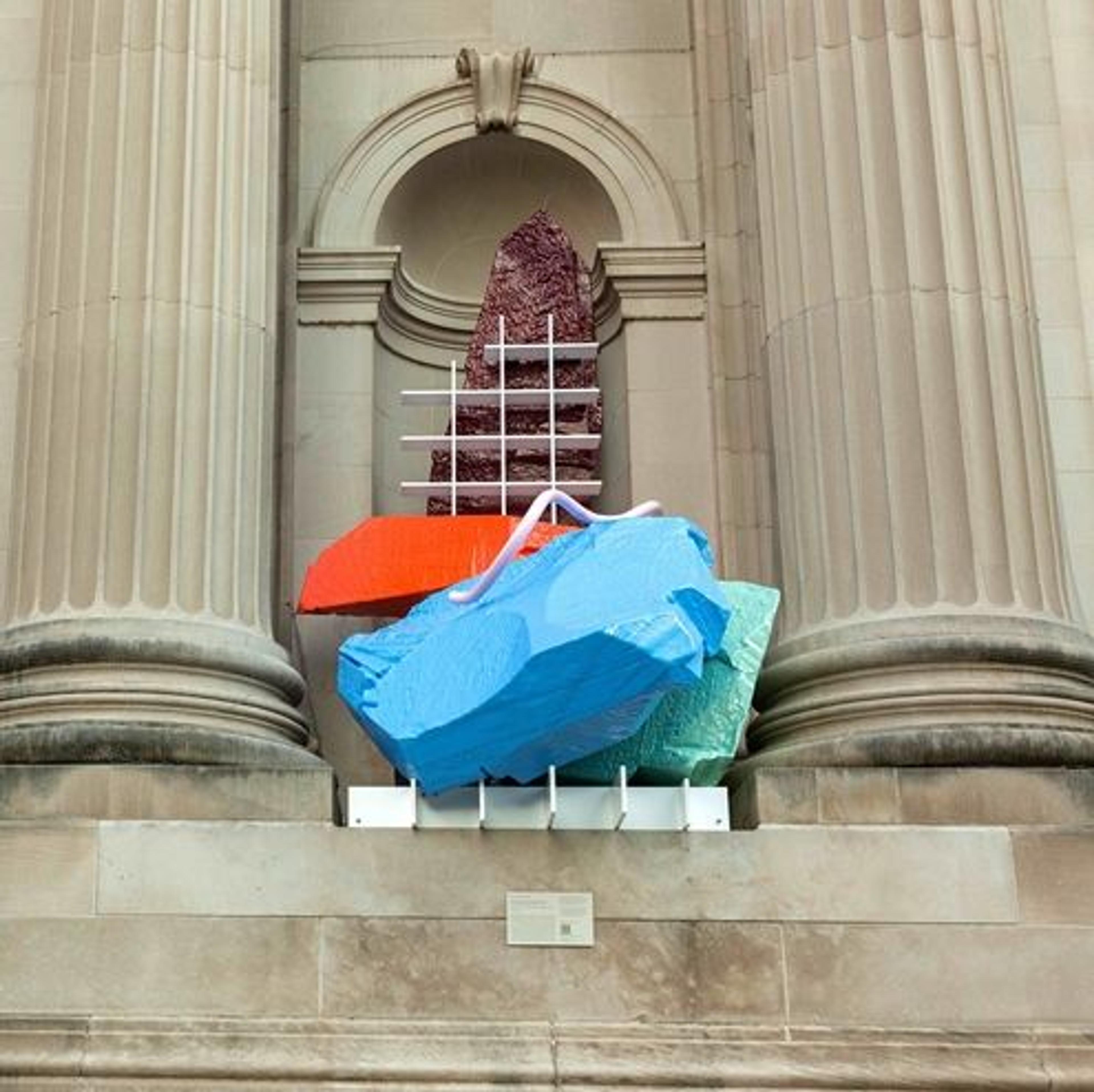 A sculpture of brightly colored rocks and grids installed between two neutral pillars.