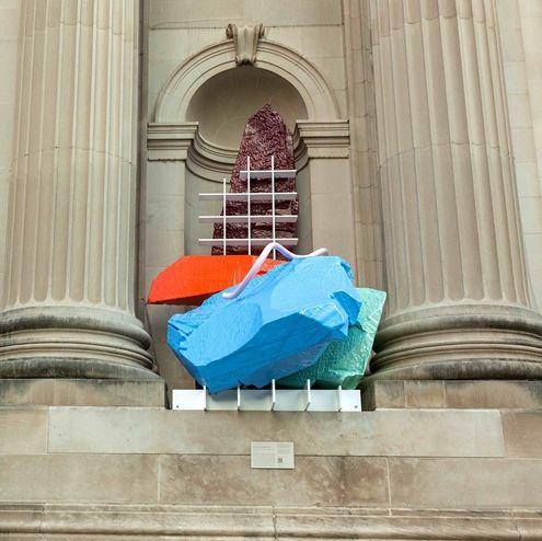 A sculpture of brightly colored rocks and grids installed between two neutral pillars.