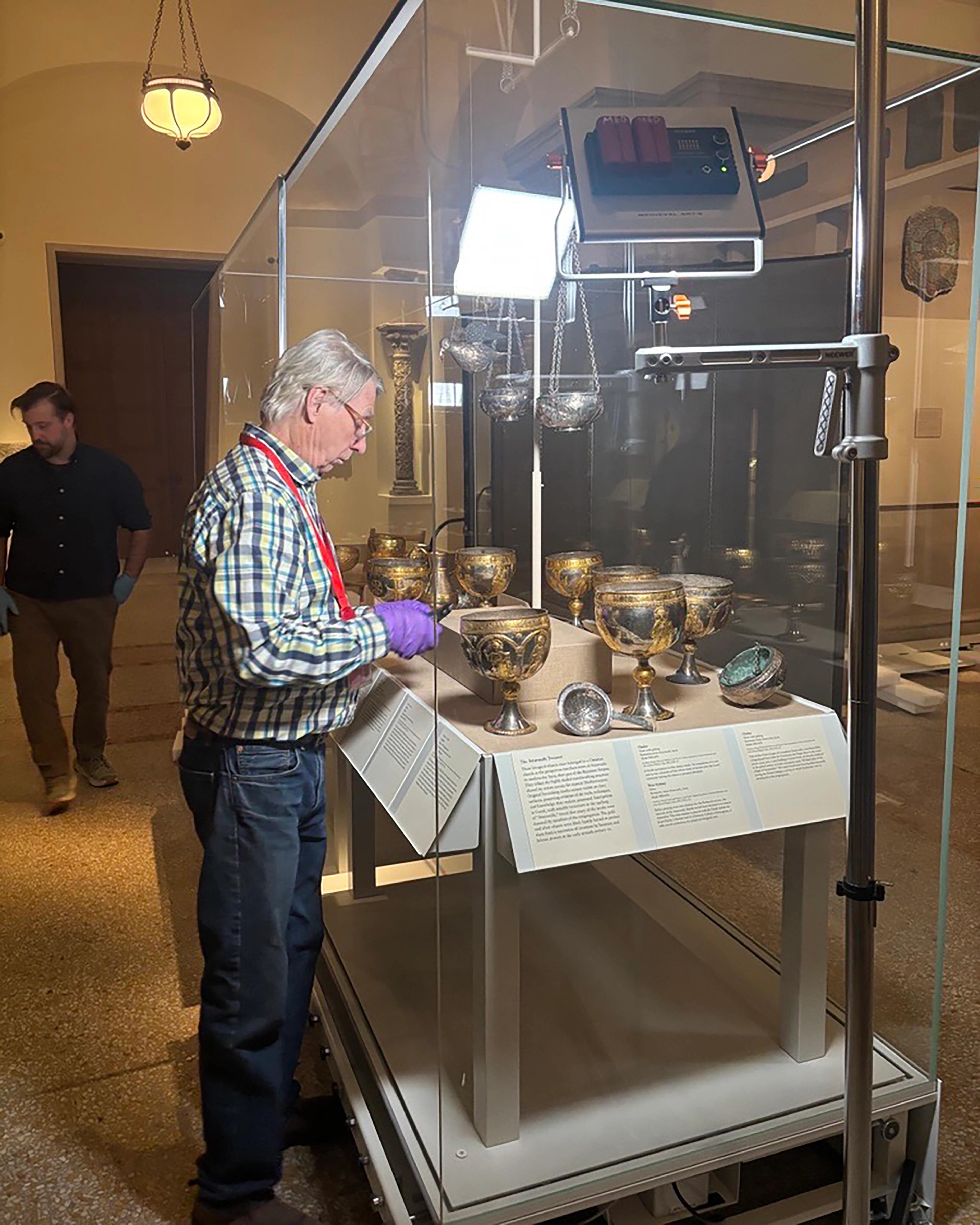 A museum employee carefully places a gold goblet into a display case