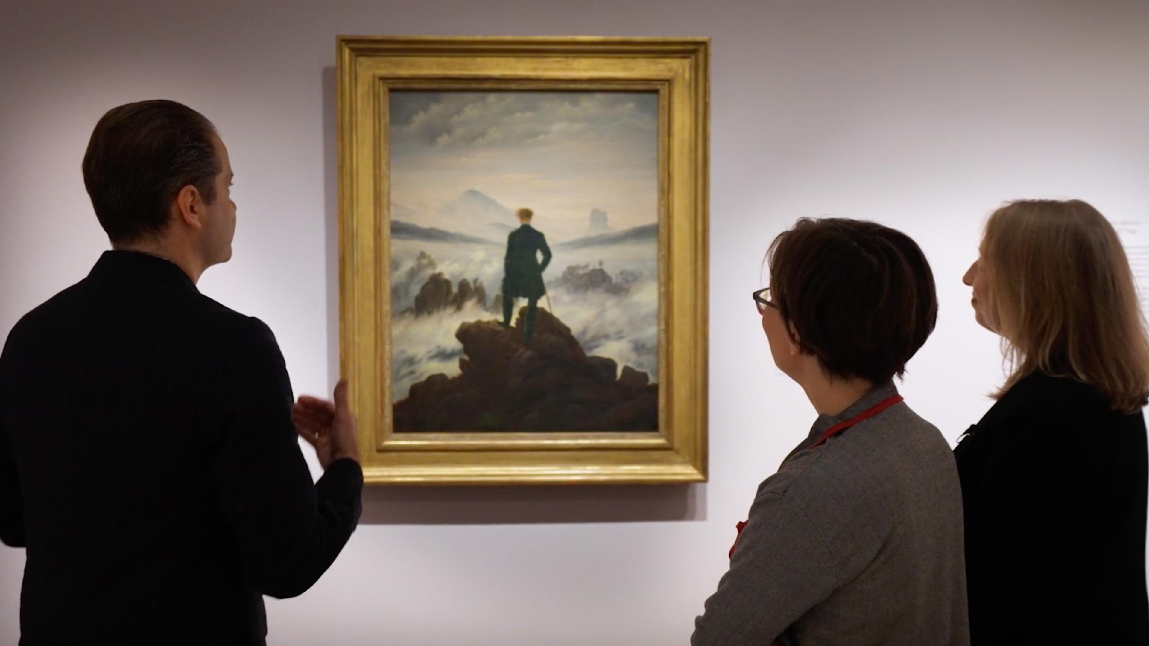 The people standing together in a gallery with hard hanging from the wall, facing them. 