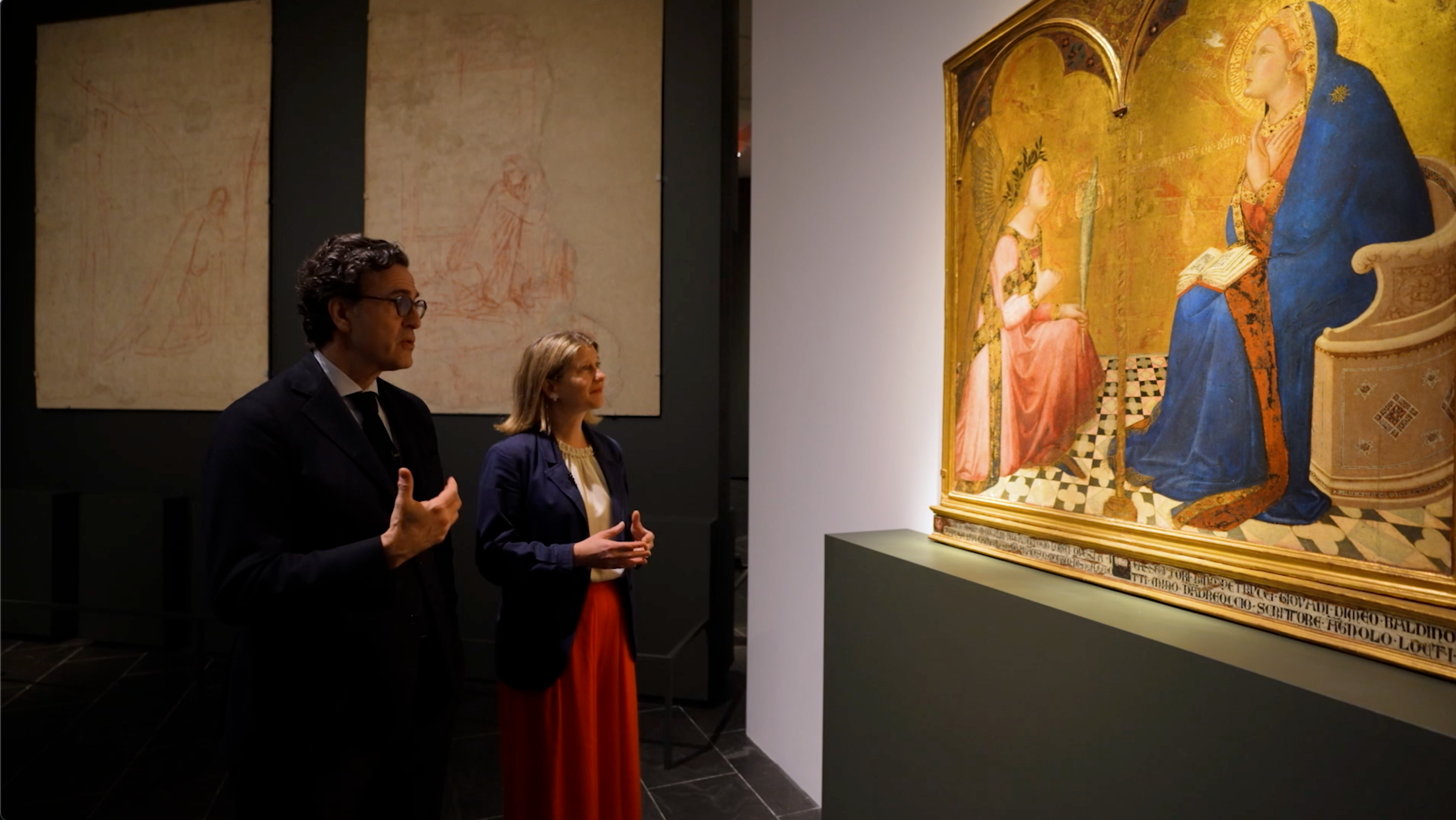A man and women stand in front of a large painting. The painting is well lit and the people are in shadow.