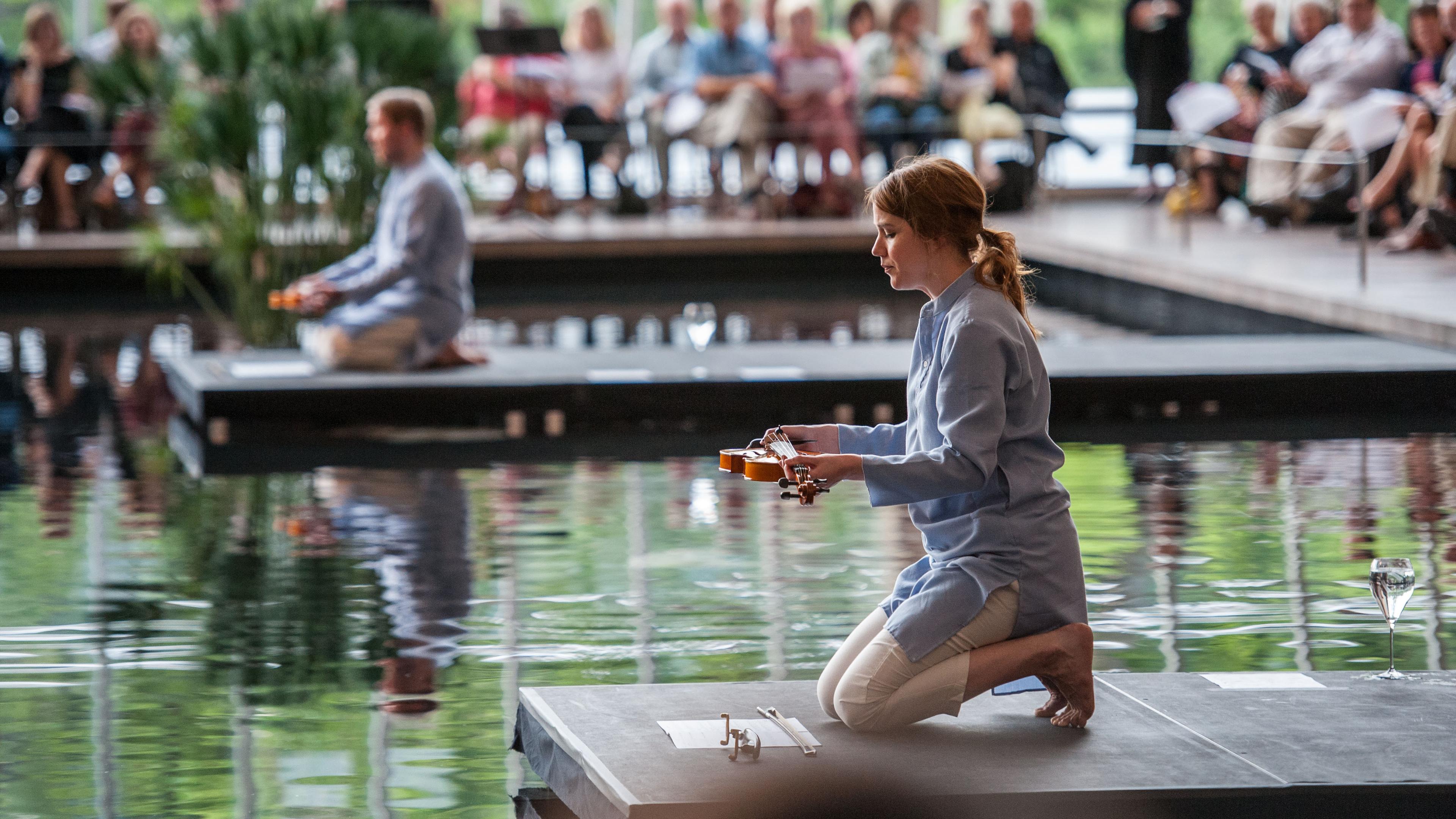 Two people holding musical instruments, kneeling on platforms over the reflecting pool in the Temple of Dendur