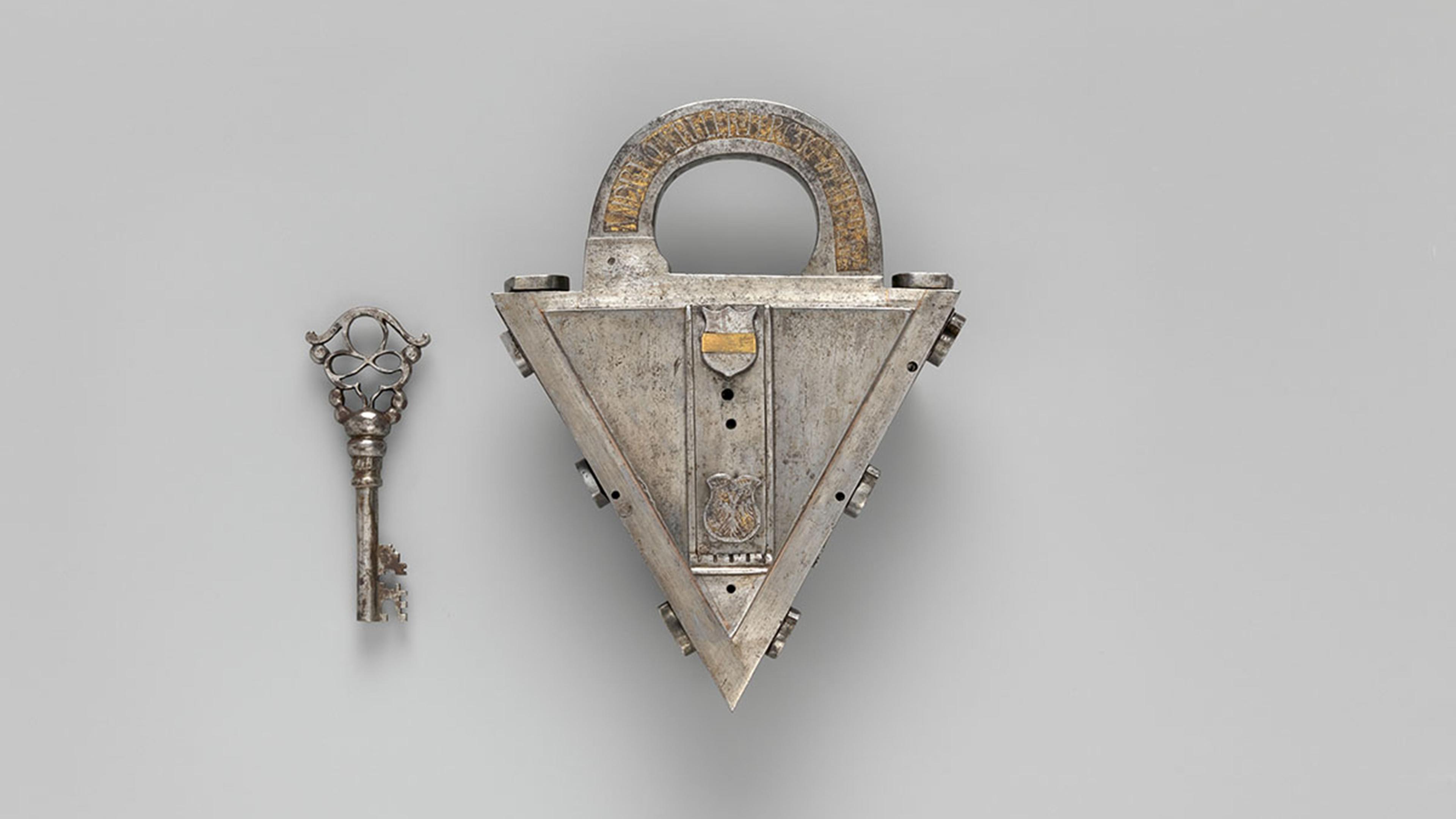 A triangular metallic lock with intricate engravings, paired with an elaborate, matching key featuring a decorative, openwork handle.