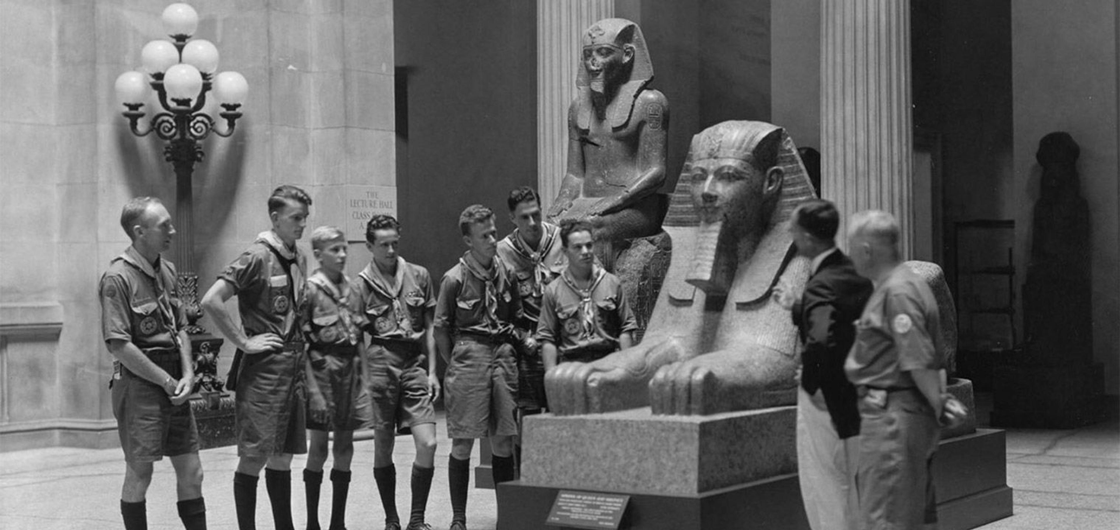 Black-and-white historical photograph of a group of uniformed boys standing in front of a Sphinx statue.