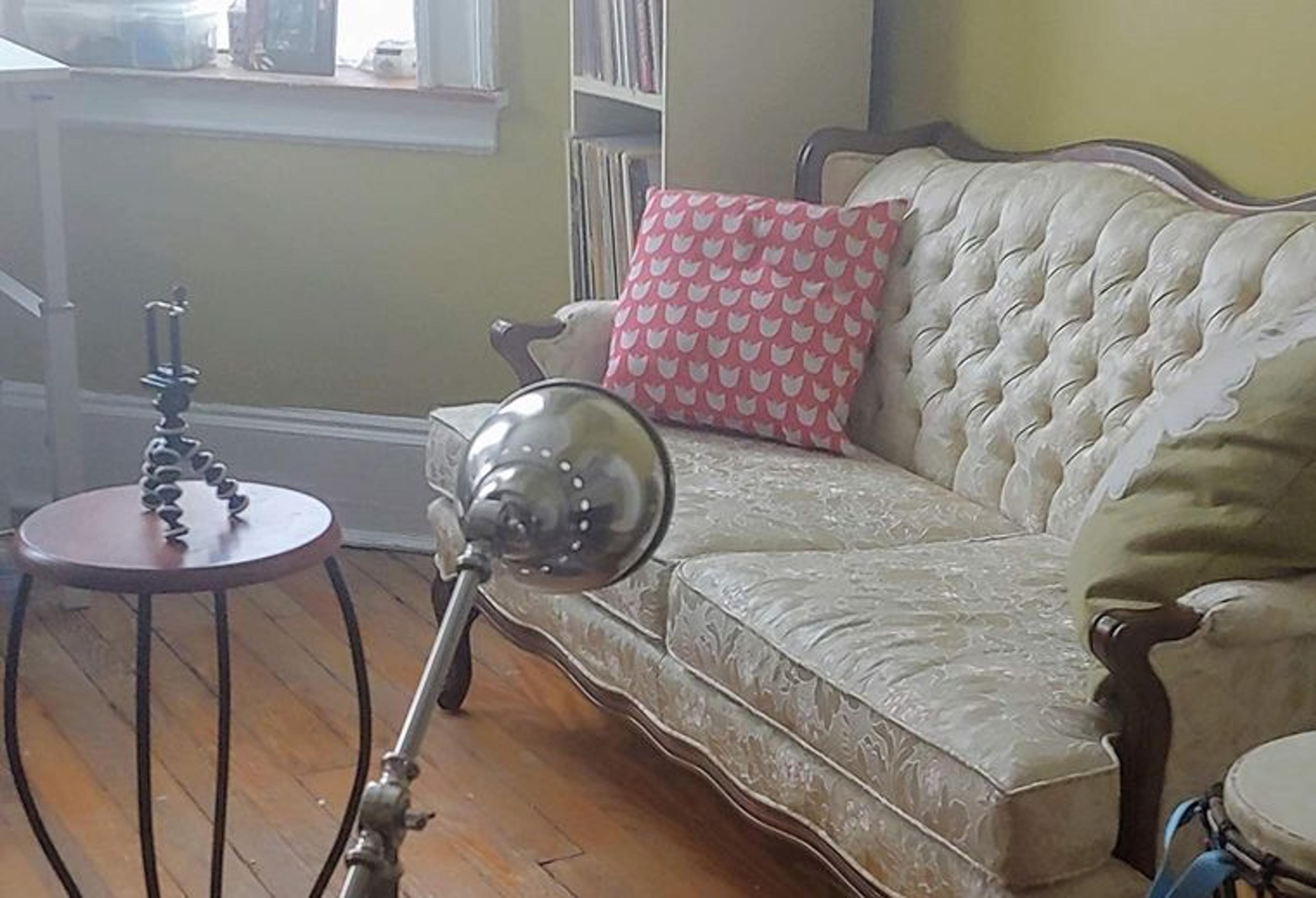 Photo of a living room with a small tripod on a table and a lamp pointed at a couch.