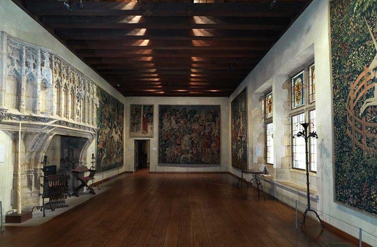 A gallery at The Met Cloisters with wood floors and ceilings and floor to ceiling tapestries on three of the walls.