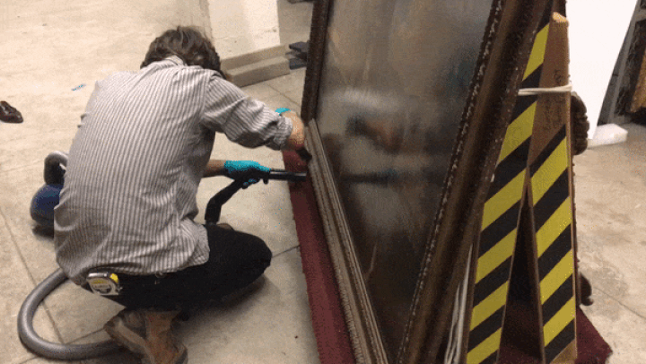 Animated image of a technician dusting a painting's frame