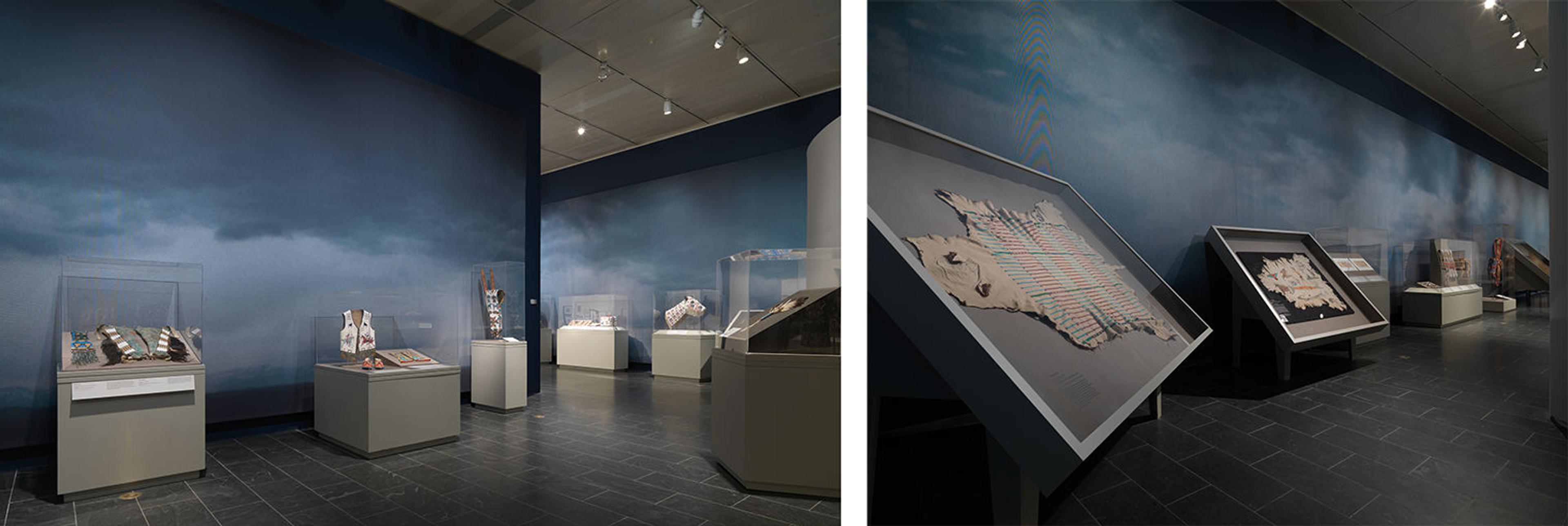 Gallery view from Plains Indians. Indigenous artworks are displayed in glass cases against a wallpaper of blue clouds.