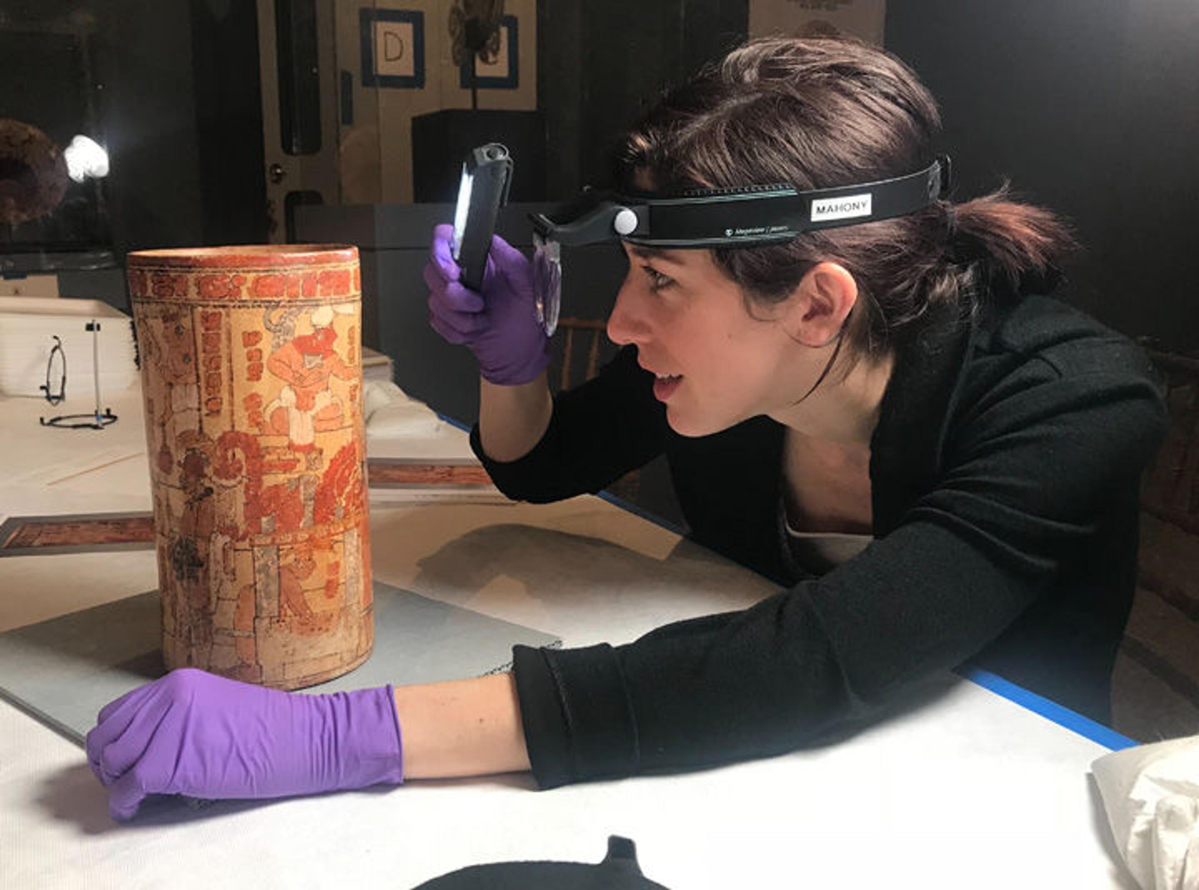 A woman studies an ancient Maya vase using light in a conservation studio