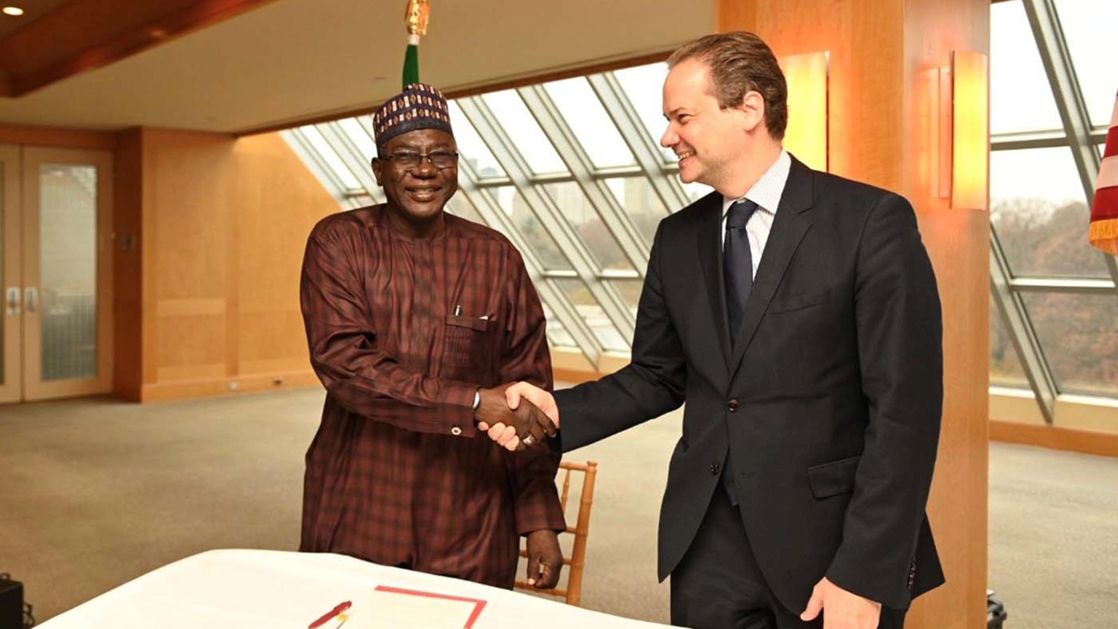 Two men standing in front of a desk shaking hands and smiling.