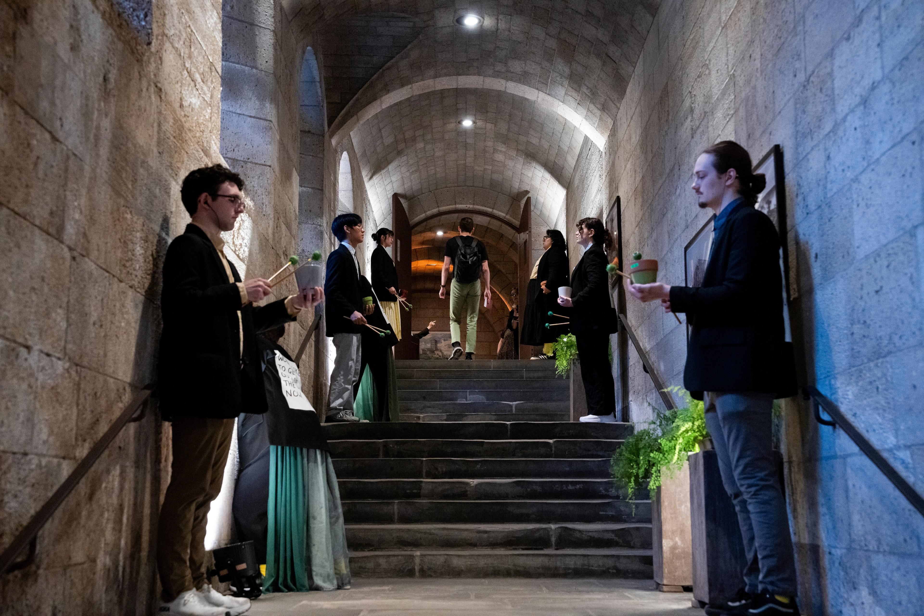 Percussionists line a Met Cloister's hallway, holding flower pots and mallets.