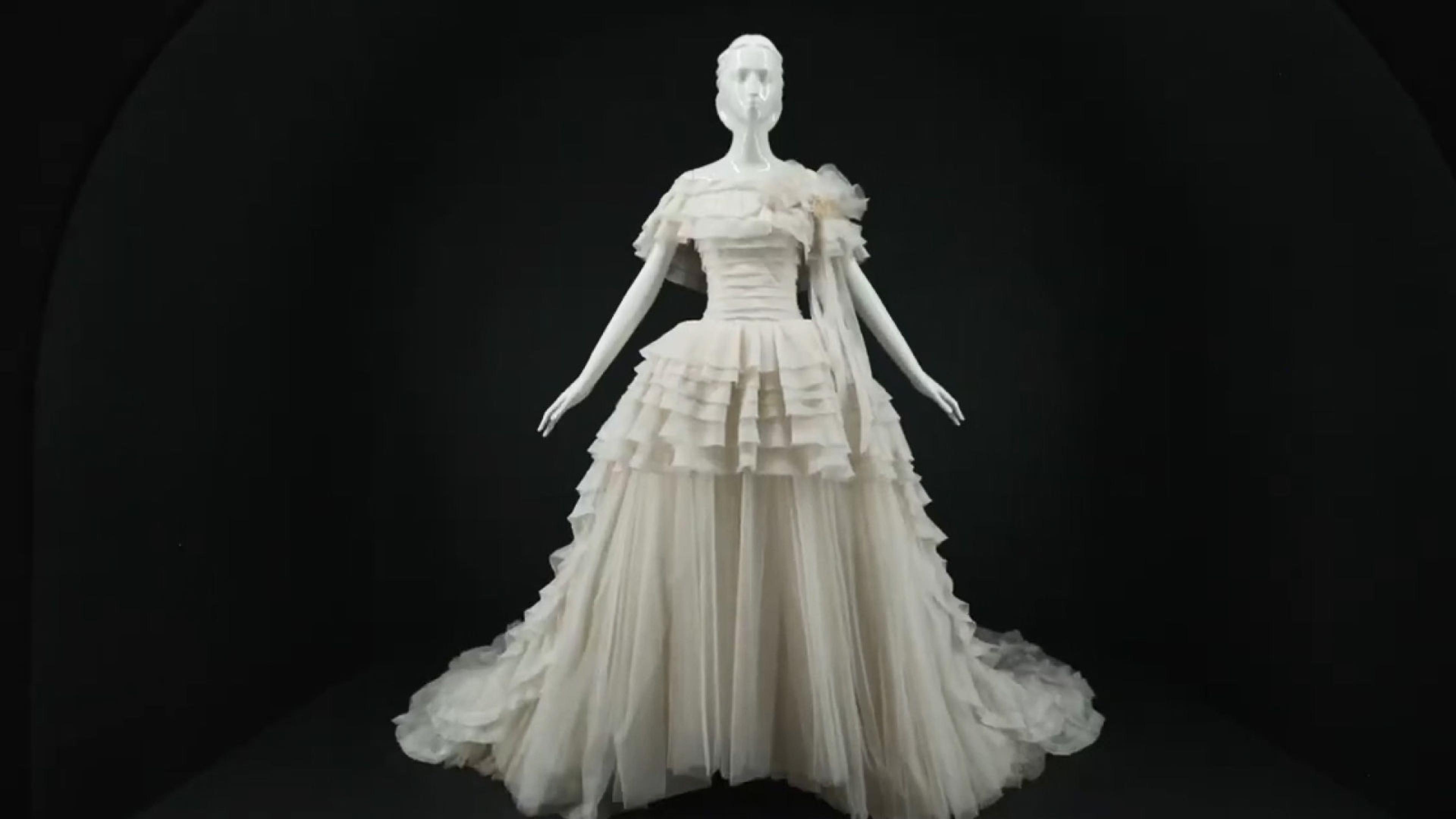 White mannequin wearing a white dress designed by Karl Lagerfeld against a pitch-black backdrop.