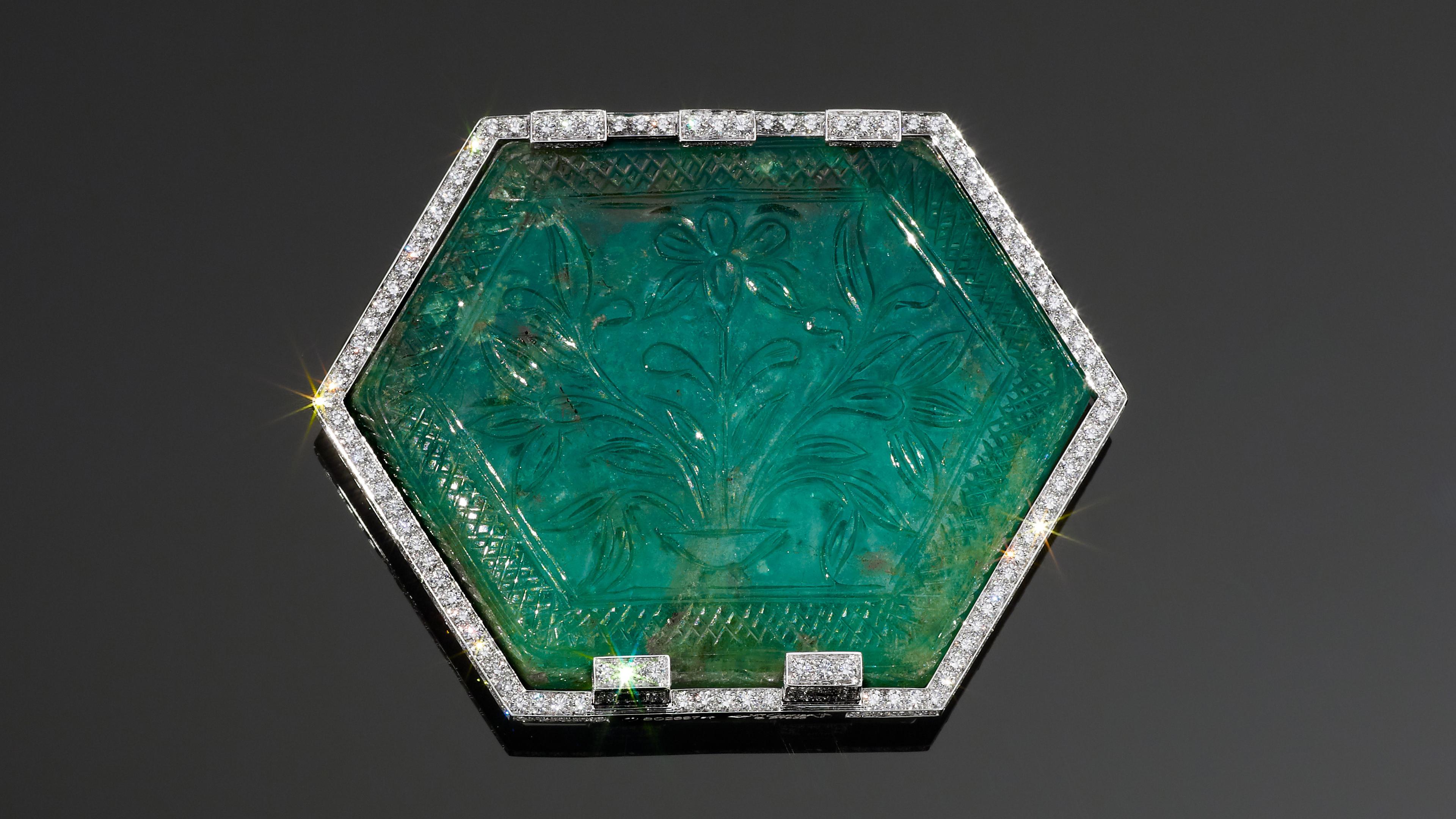 Close up of a hexagonal green stone carved with floral motifs, surrounded by a border of diamonds