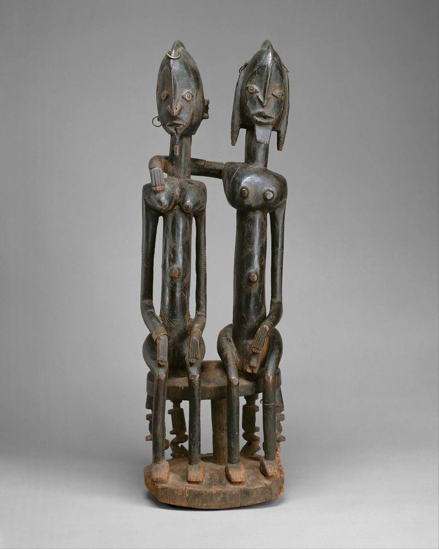 Sculpture of couple sitting on a round bench, with one figure holding their arm over the other figure's shoulder.