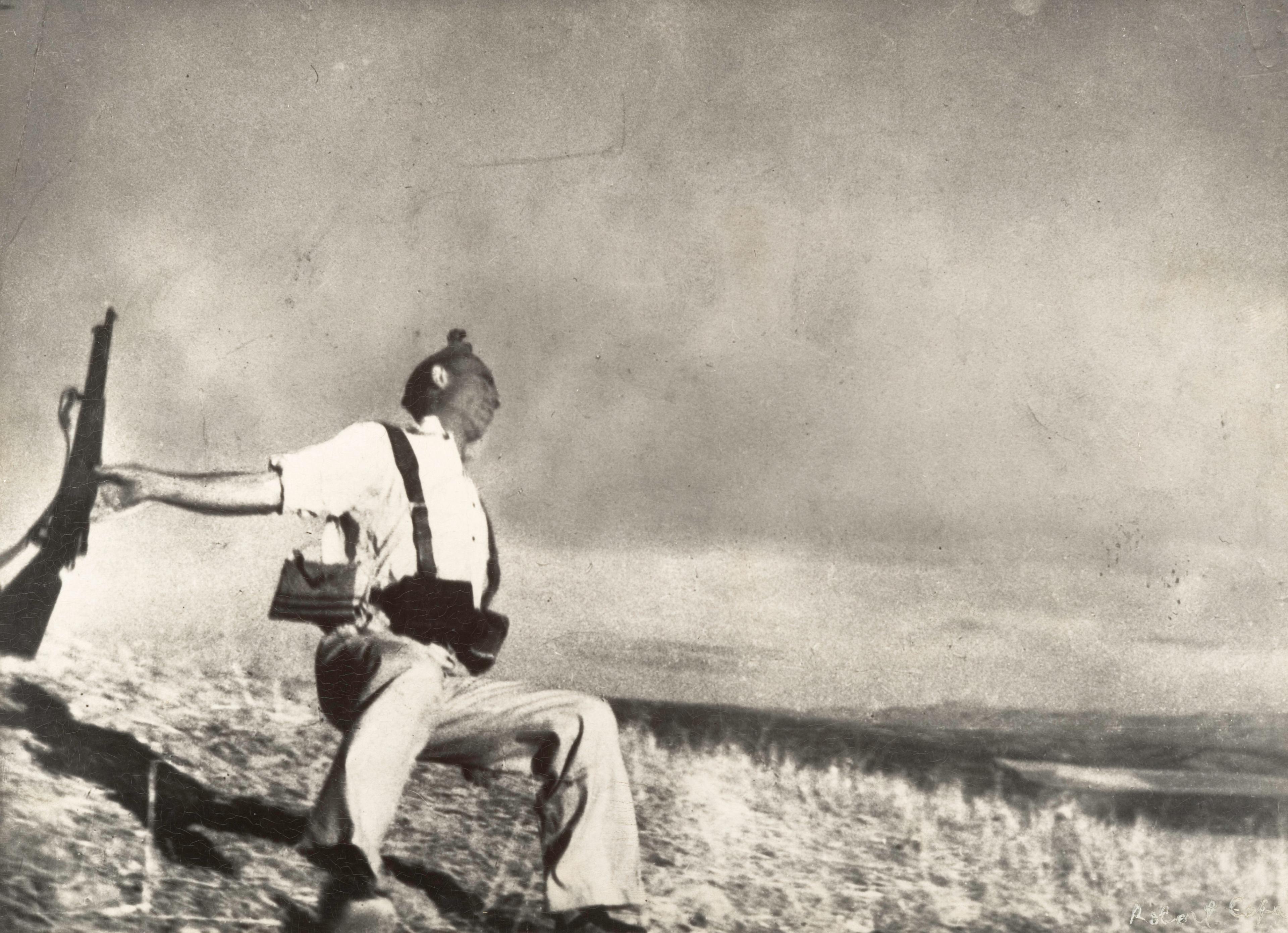 Black and white photograph of a man falling to the ground holding a rifle.