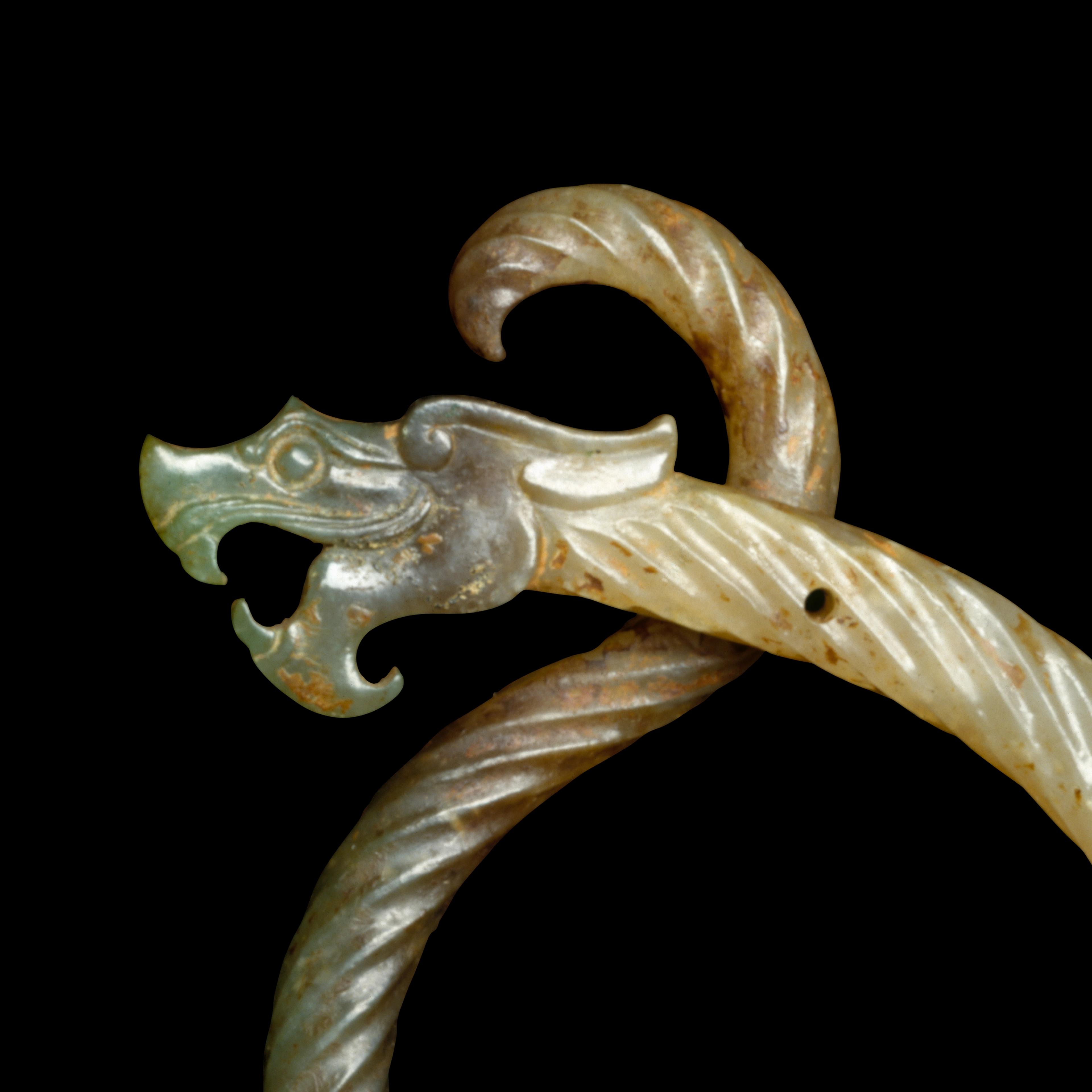 A carved jade ornament featuring a dragon's head with an open mouth and spiral body against a black background.
