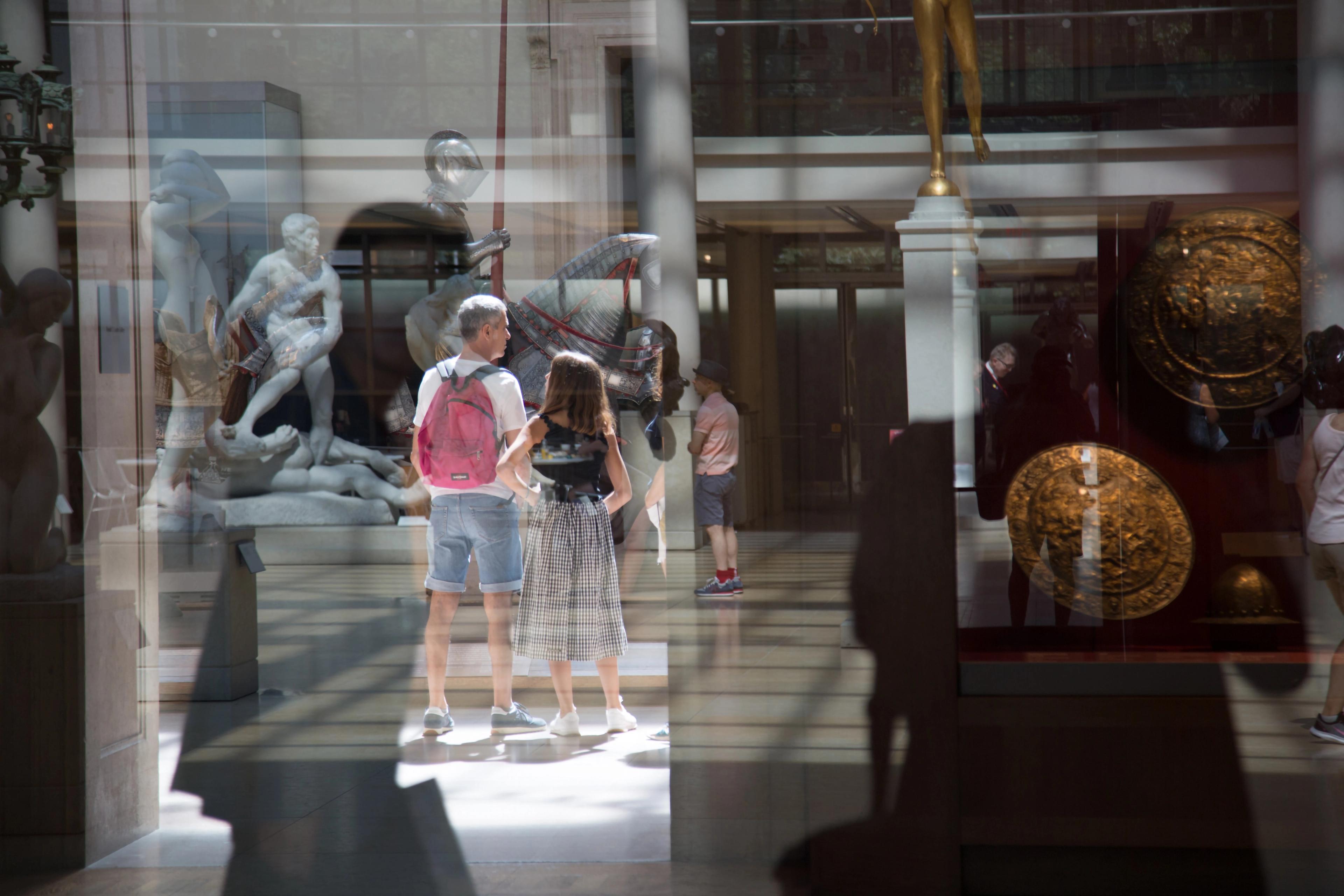 Photograph reflecting stone sculptures, medieval armor, a round shield, and Museum patrons  in the sunlit Engelhard Court.