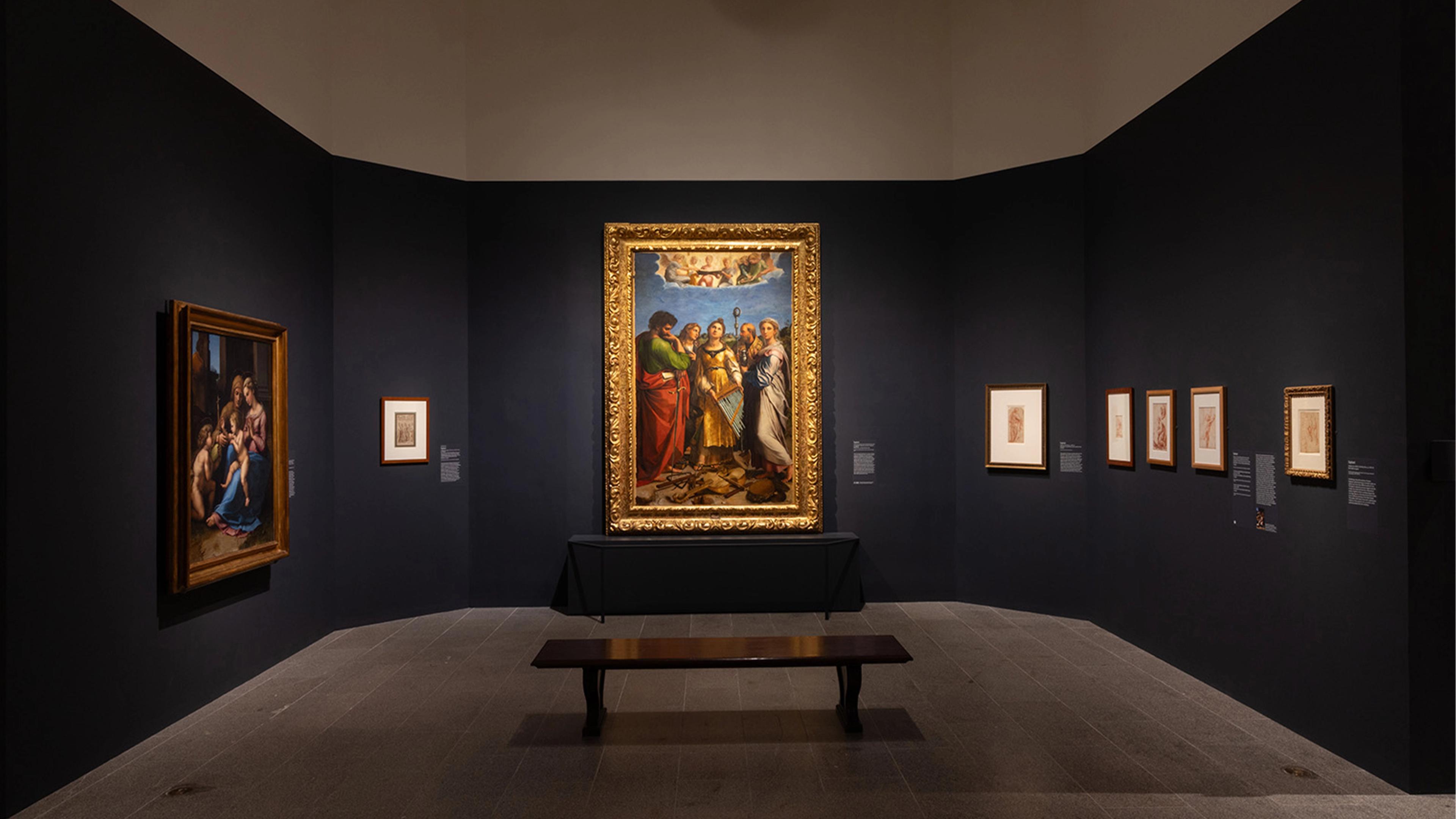 Museum gallery with dim lighting features a central large, ornate framed painting surrounded by smaller artworks on dark walls.