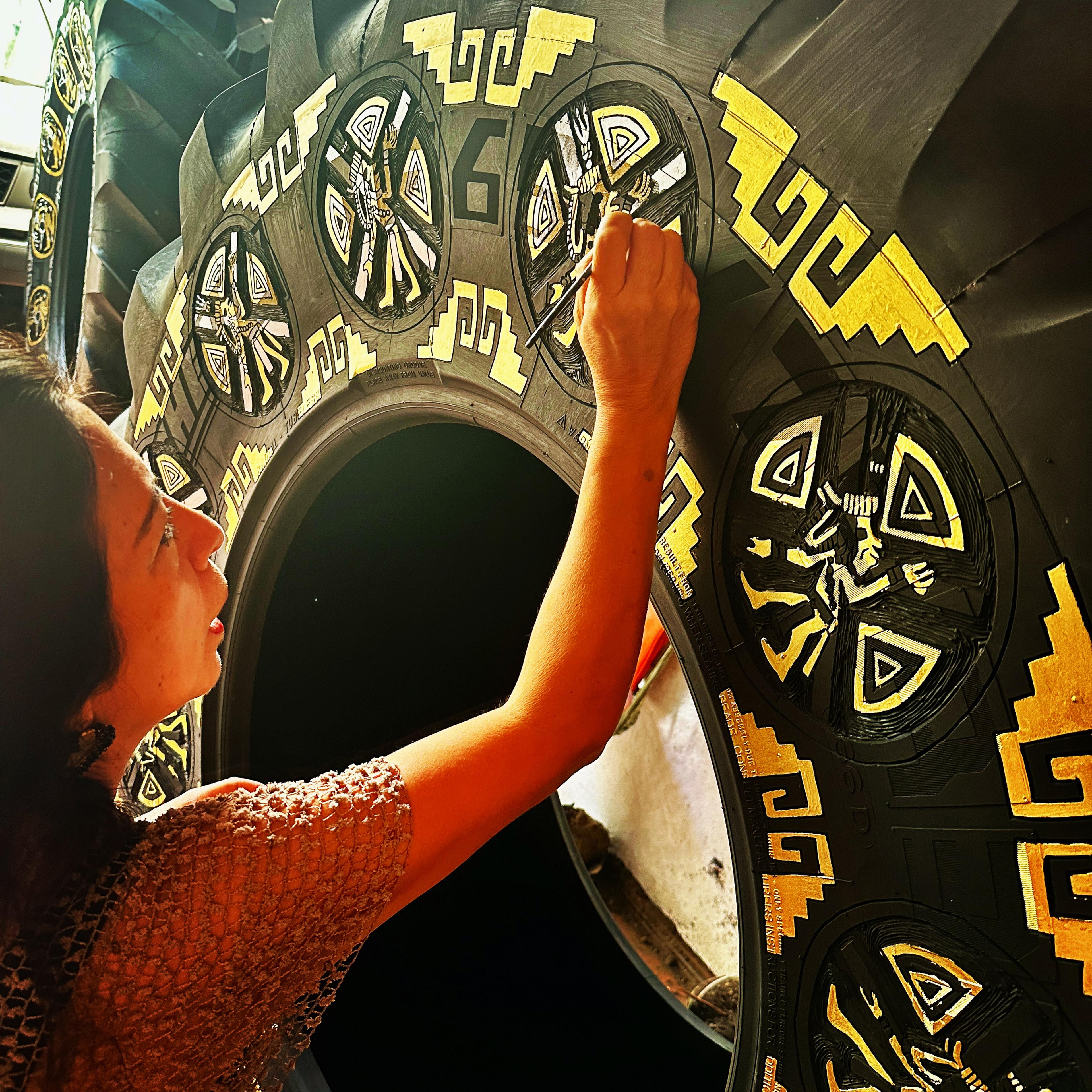Betsabeé Romero painting a large tire with bright yellow geometric designs that reference and evoke ancient motifs.