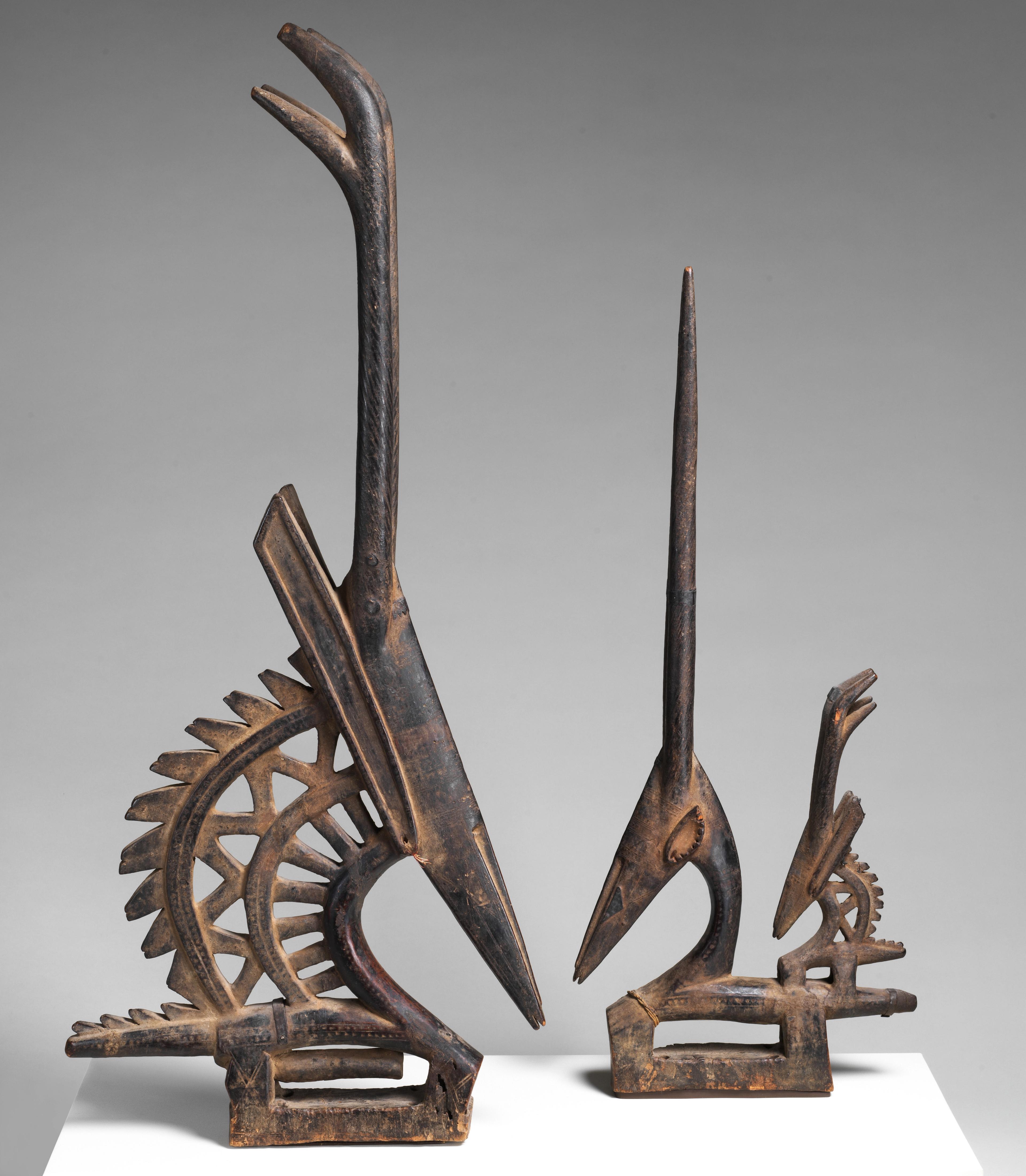 Two carved wood and metal headdresses in the shape of antelopes, one larger than the other.