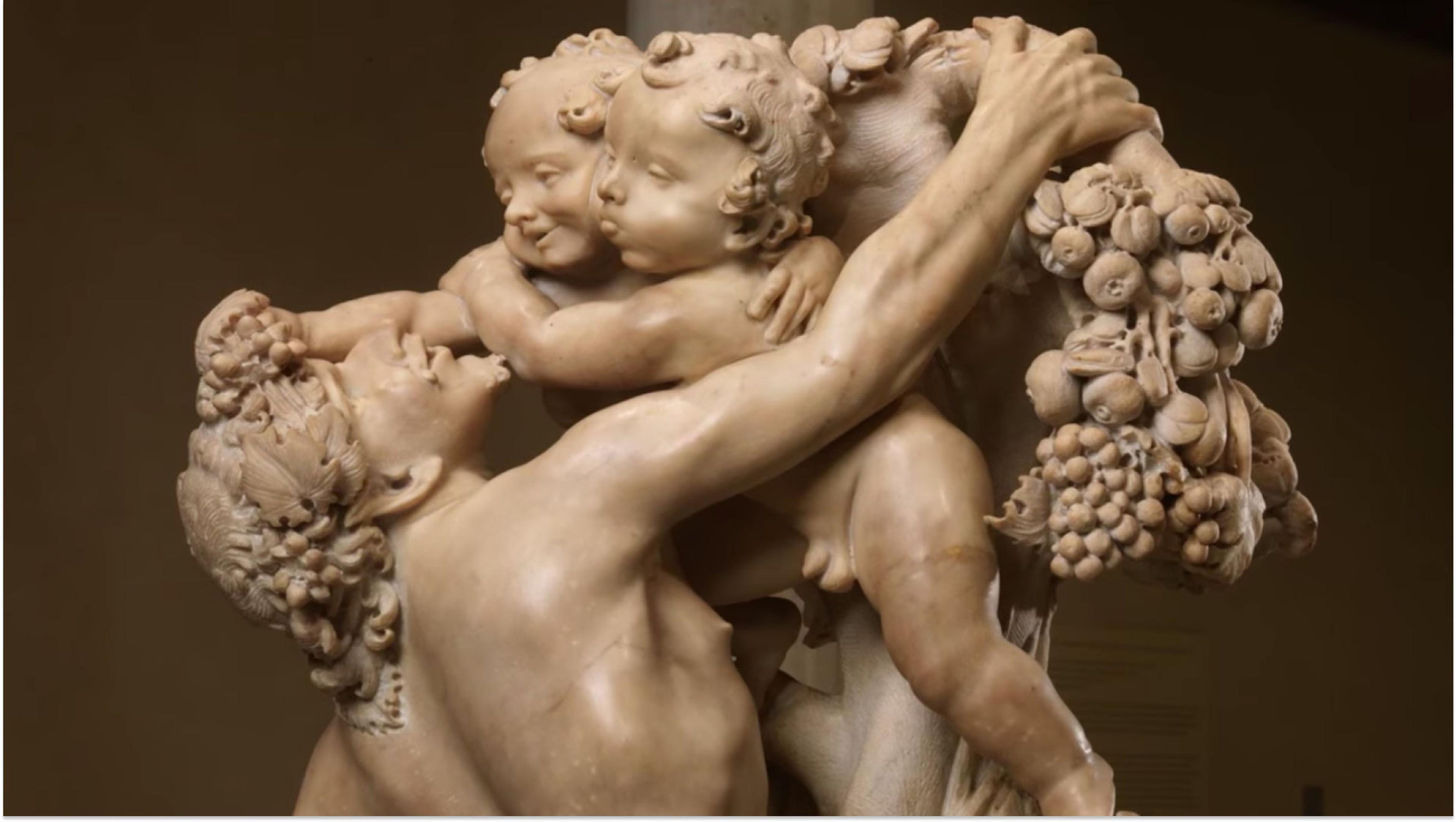 Marble sculpture depicts a satyr reaching up to pick grapes as naked sprites push him back.
