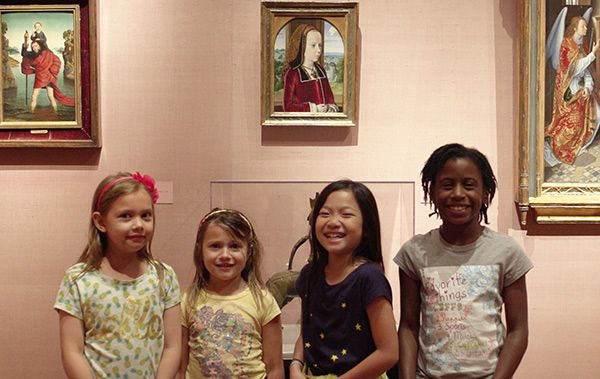 Group of four smiling children in front of a gallery wall.