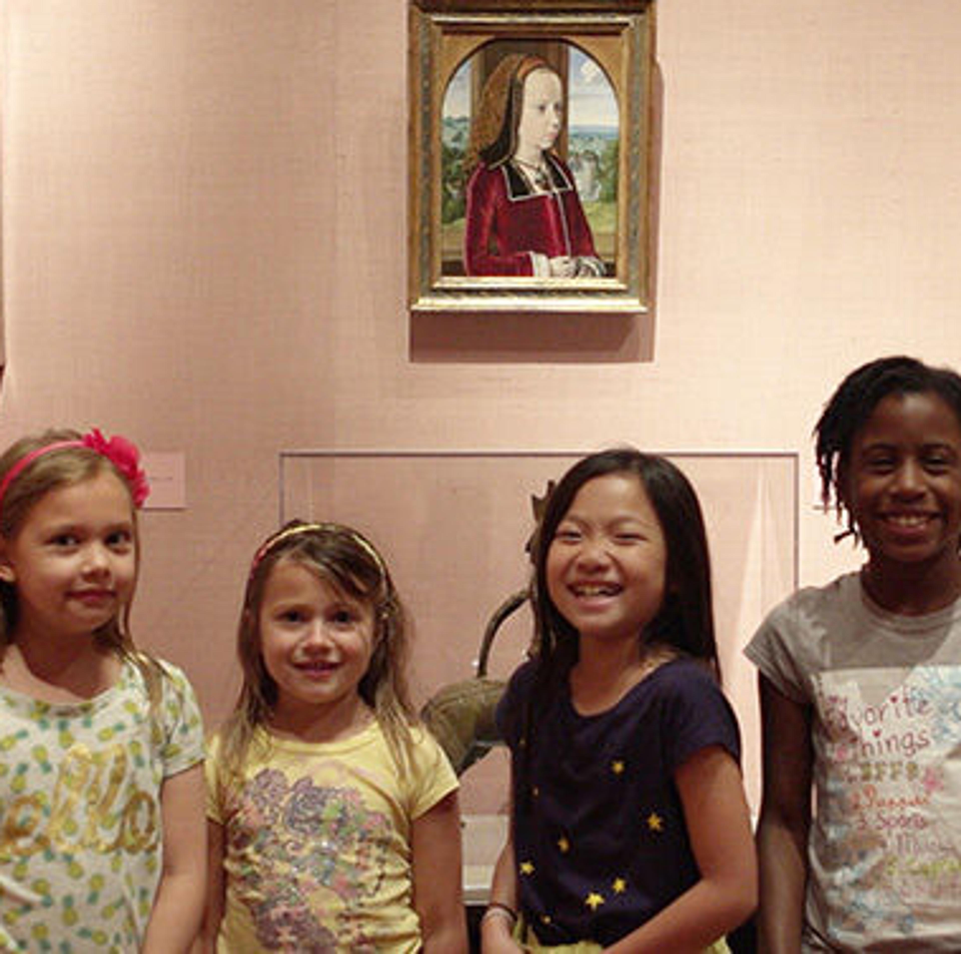 Group of four smiling children in front of a gallery wall.