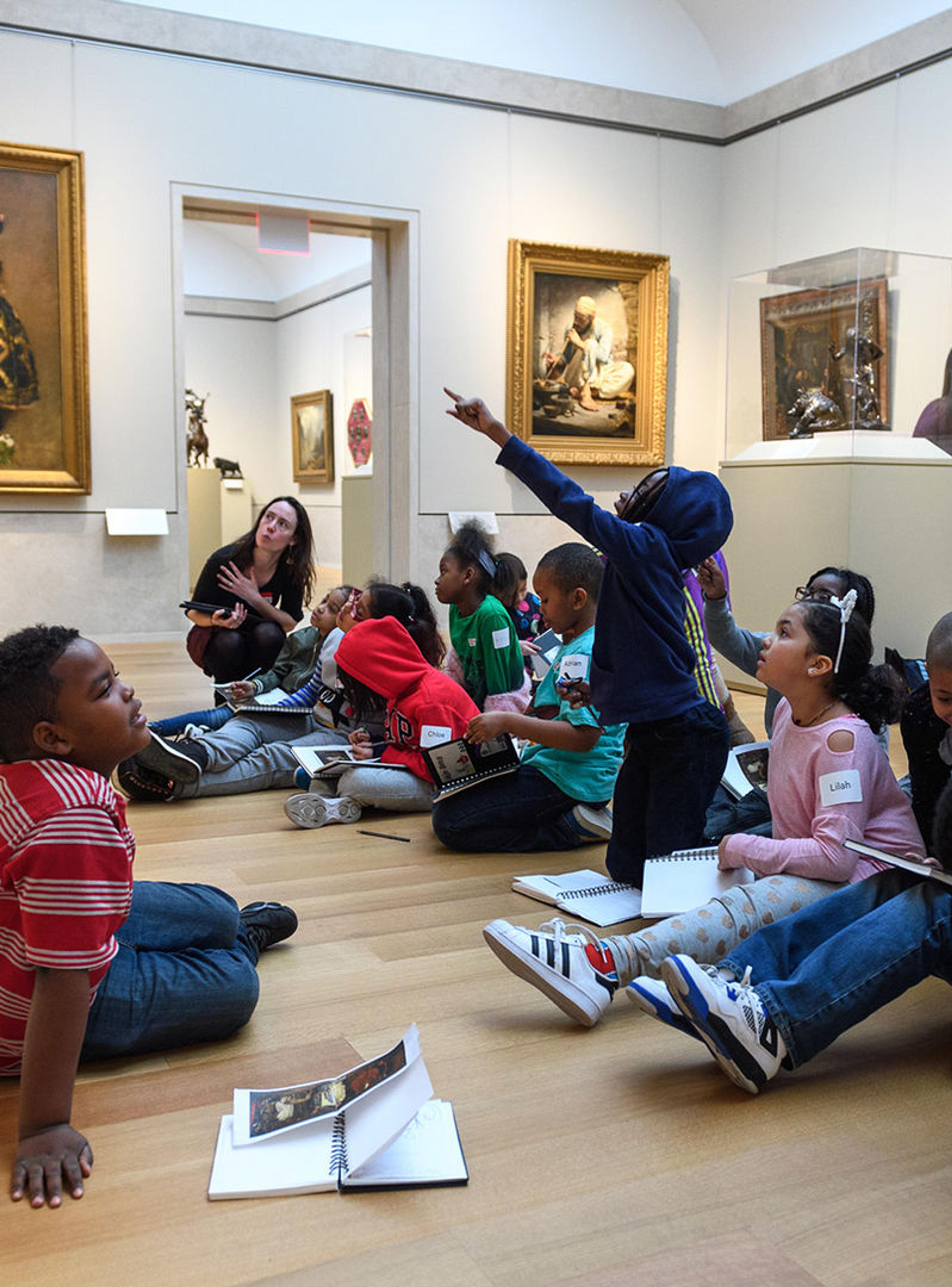 A group of children sitting on the floor and pointing to works in The Met's American Wing.