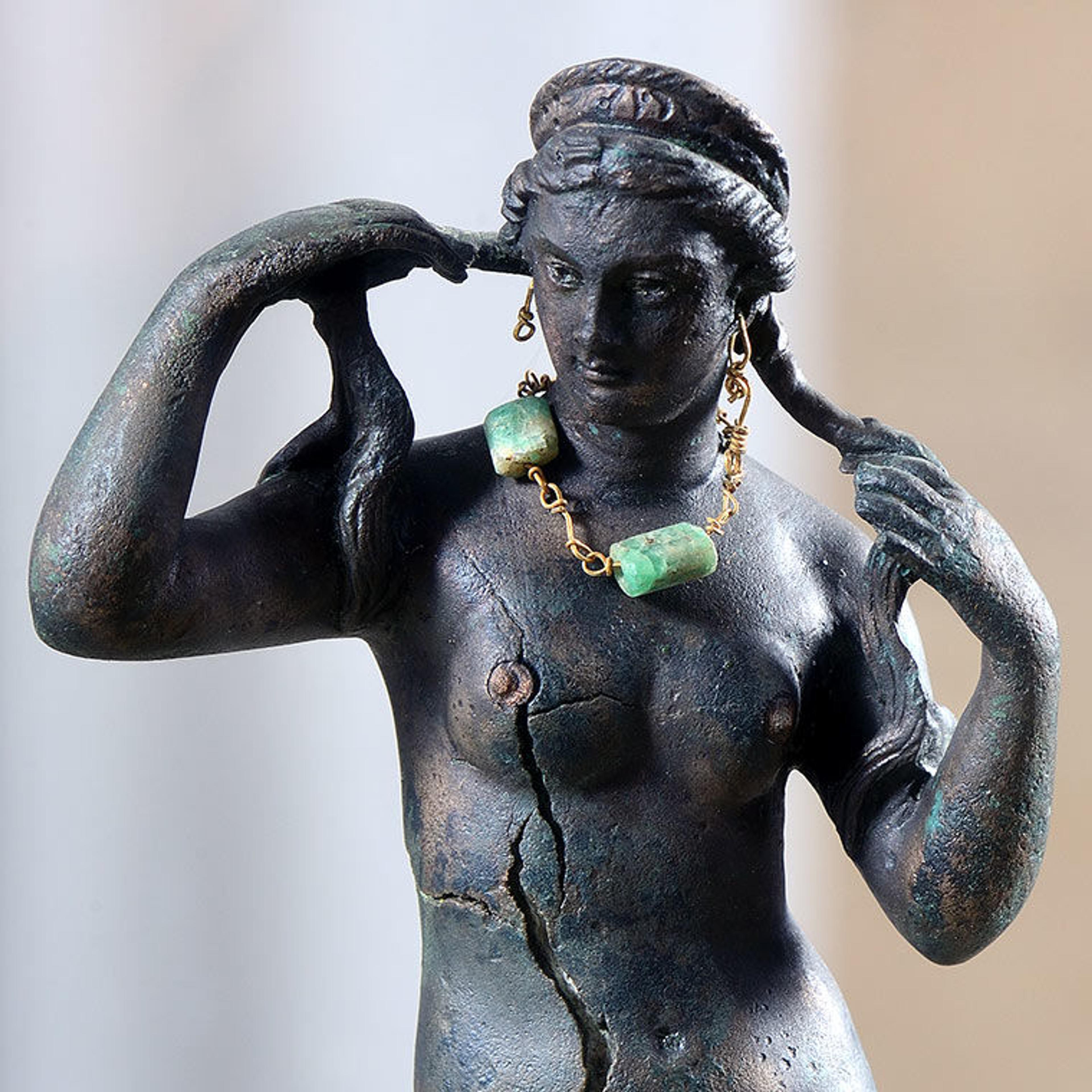 Detail of Aphrodite figurine holding her wet braids in her hands and wearing a green emerald necklace