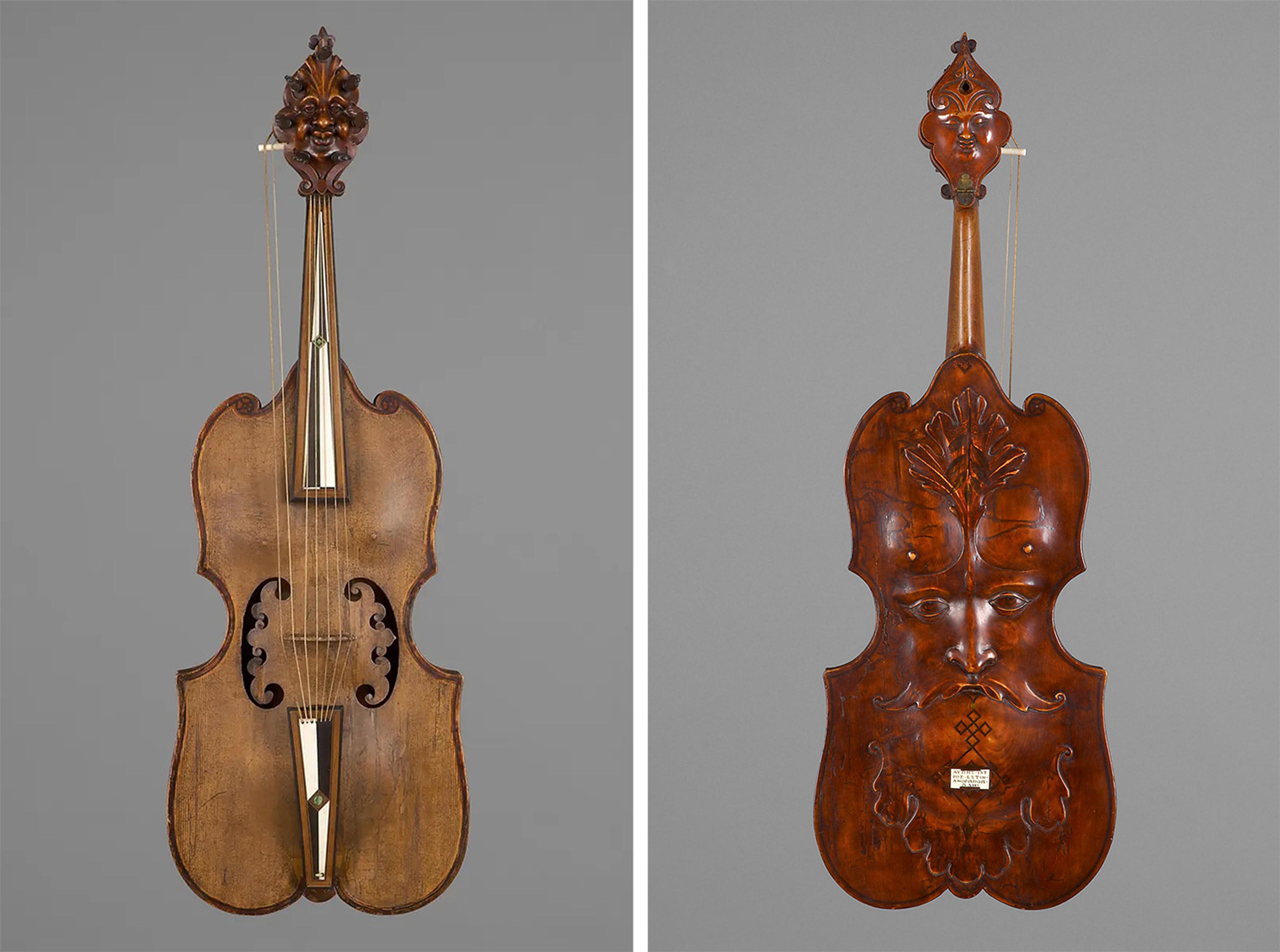 Antique string instrument with ornate carvings. The front has a classic violin shape, while the back features a carved face and leaf motif. Elegant and artistic design.