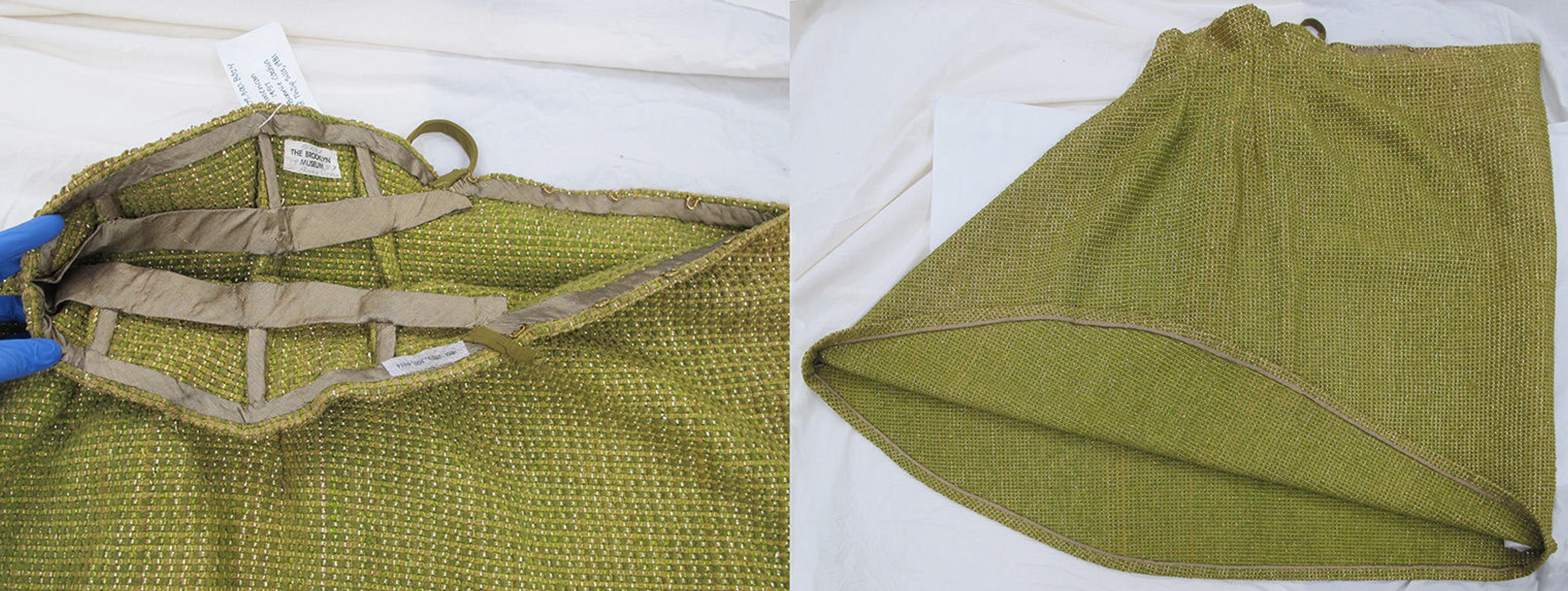 At left, an interior view of the green skirt’s waistline and center back closure, which is finished with a narrow taupe bias tape. The waist and hip areas are shaped by three darts per side, each of which is stiffened by a piece of boning encased in a taupe bias tape channel. A waist stay is sewn into the center front of the skirt and tacked to each of the six bones. The back ends of the waist stay are secured beneath the bias tape that edges the waistline. At right, the green skirt is laid flat on a table with the bias-cut center front seam towards the left and the center back fold on the right. The hem is turned up to show a one-and-a-half-inch seam allowance with the cut edge bound with taupe bias tape.