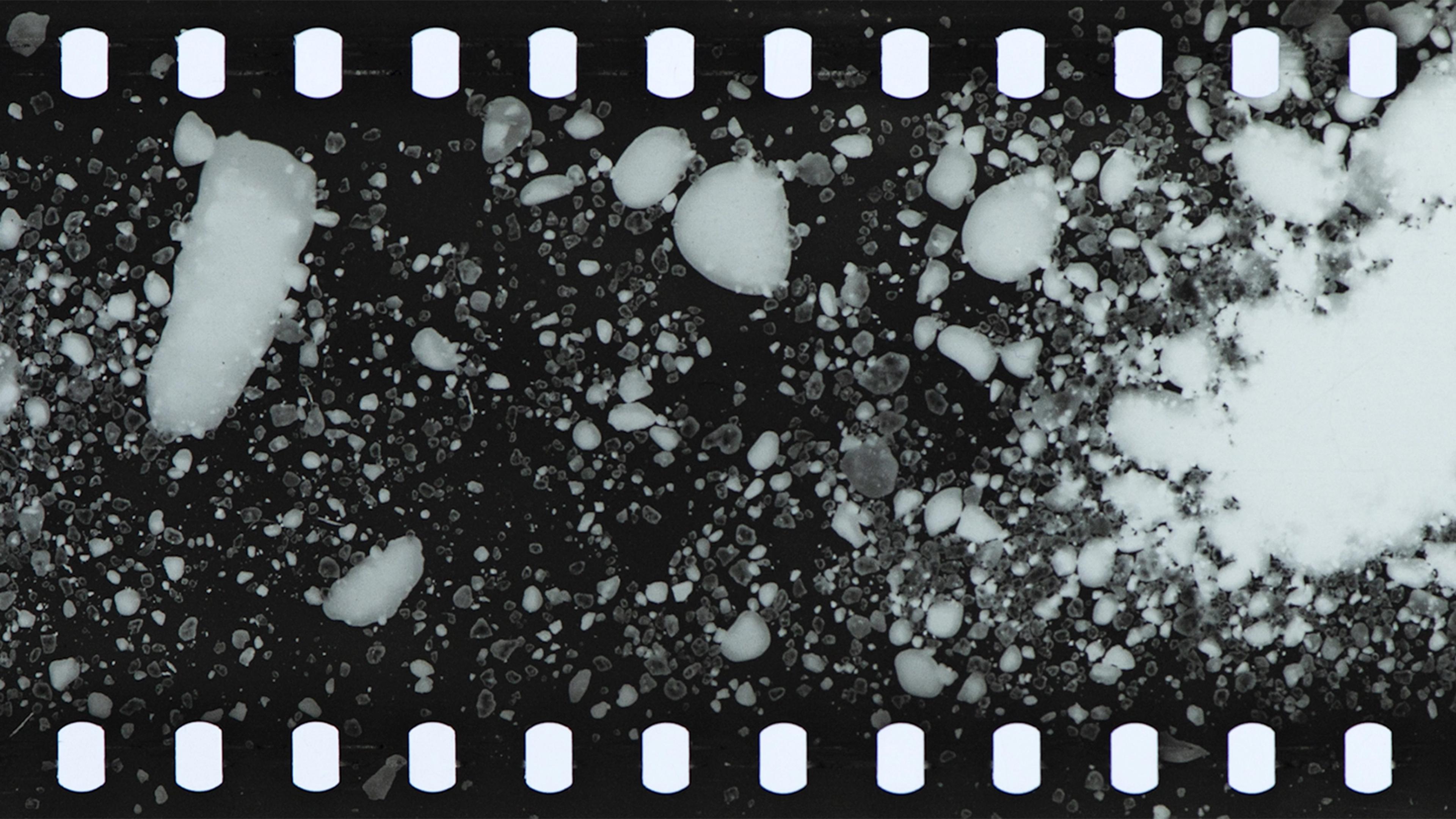 Black and white filmstrip with white forms that look like grains of salt or snow.