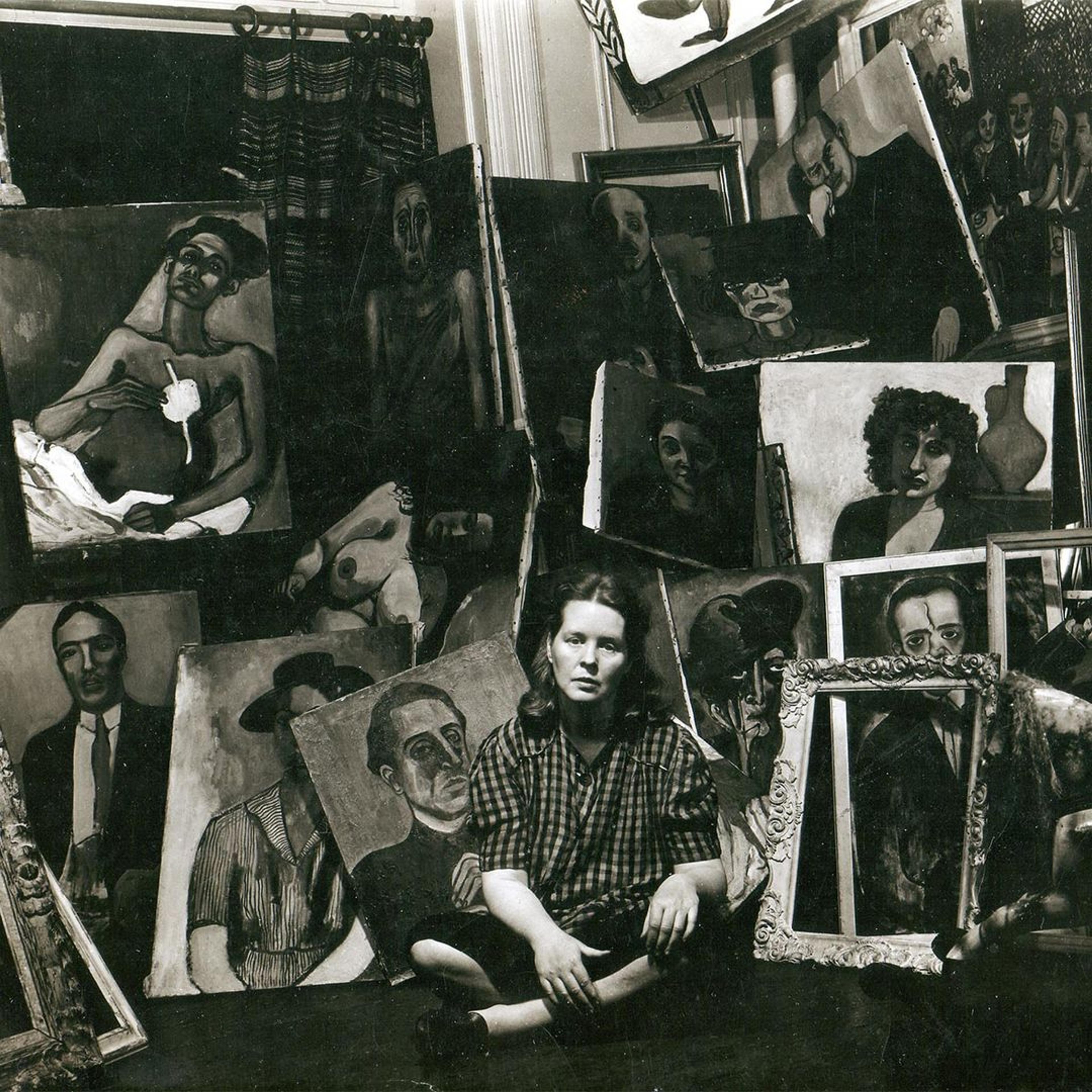 Black-and-white photograph of a seated, sad-looking woman. Behind her are empty frames and painted portraits.