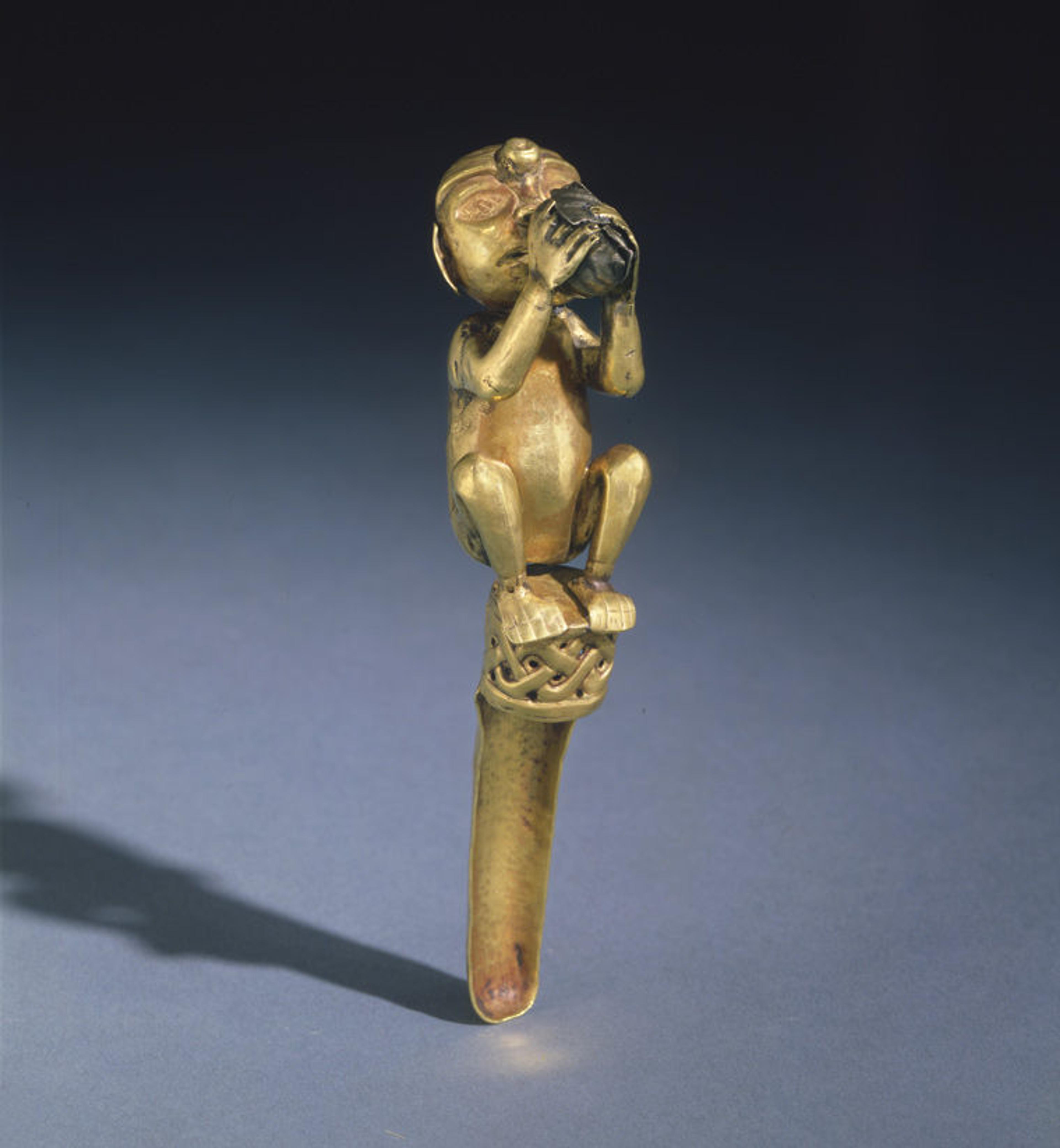 An ancient Peruvian effigy spoon made of gold and featuring a figure playing a conch trumpet