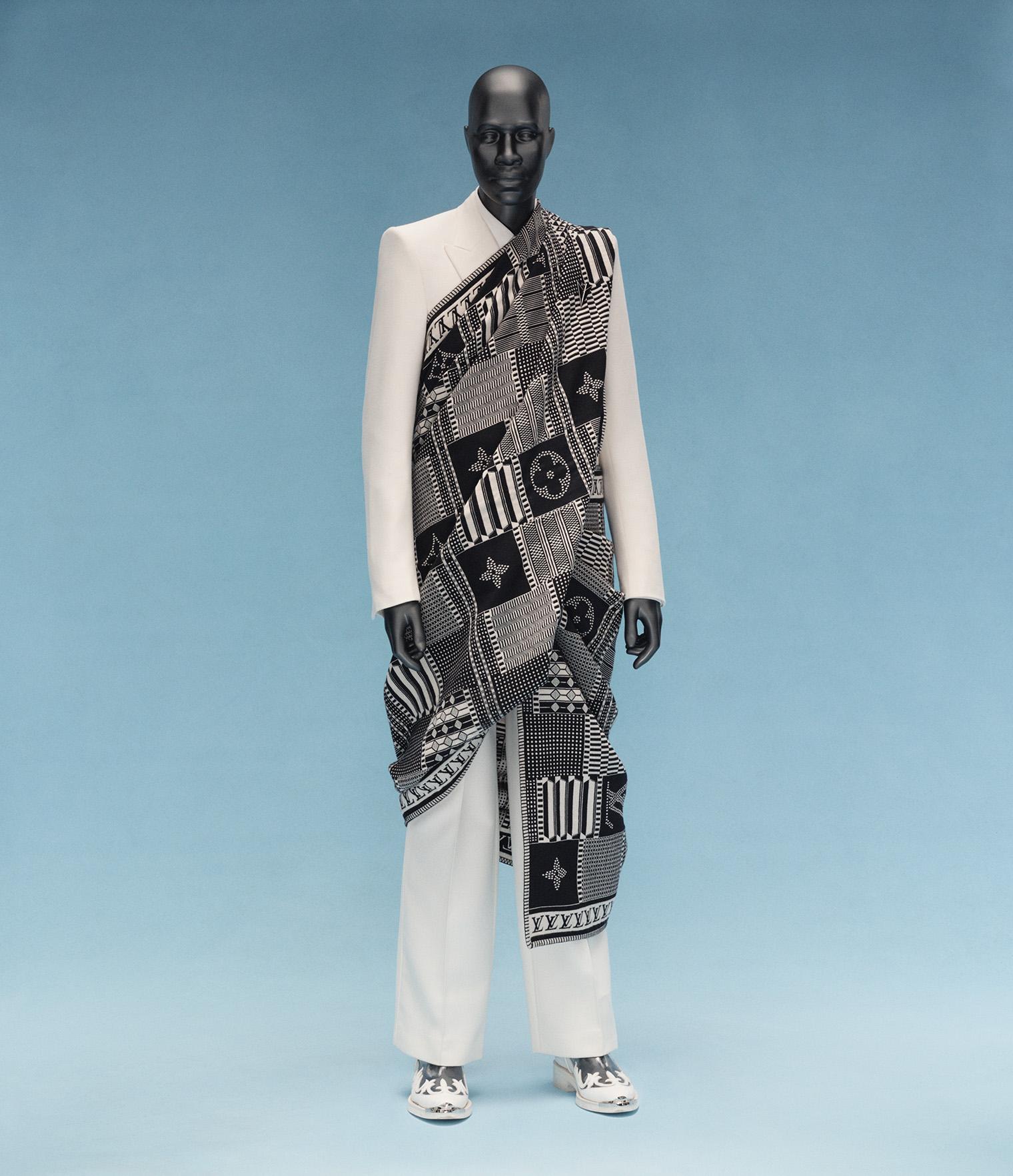 A mannequin dressed in a sleek white suit and patterned black and white fabric wrap stands against a soft blue background, exuding elegance and modernity.