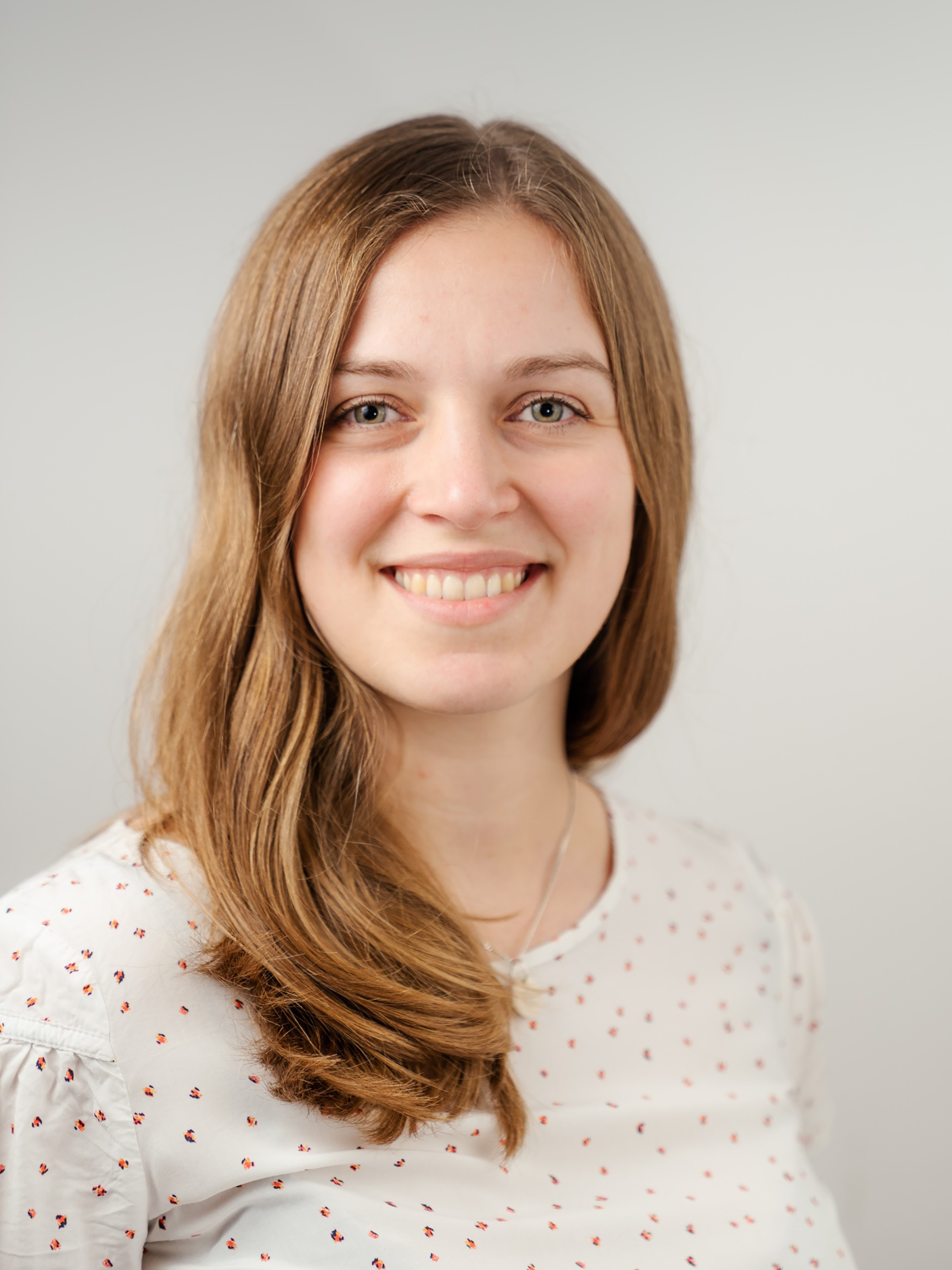 A woman with long hair in a white shirt poses against a neutral background